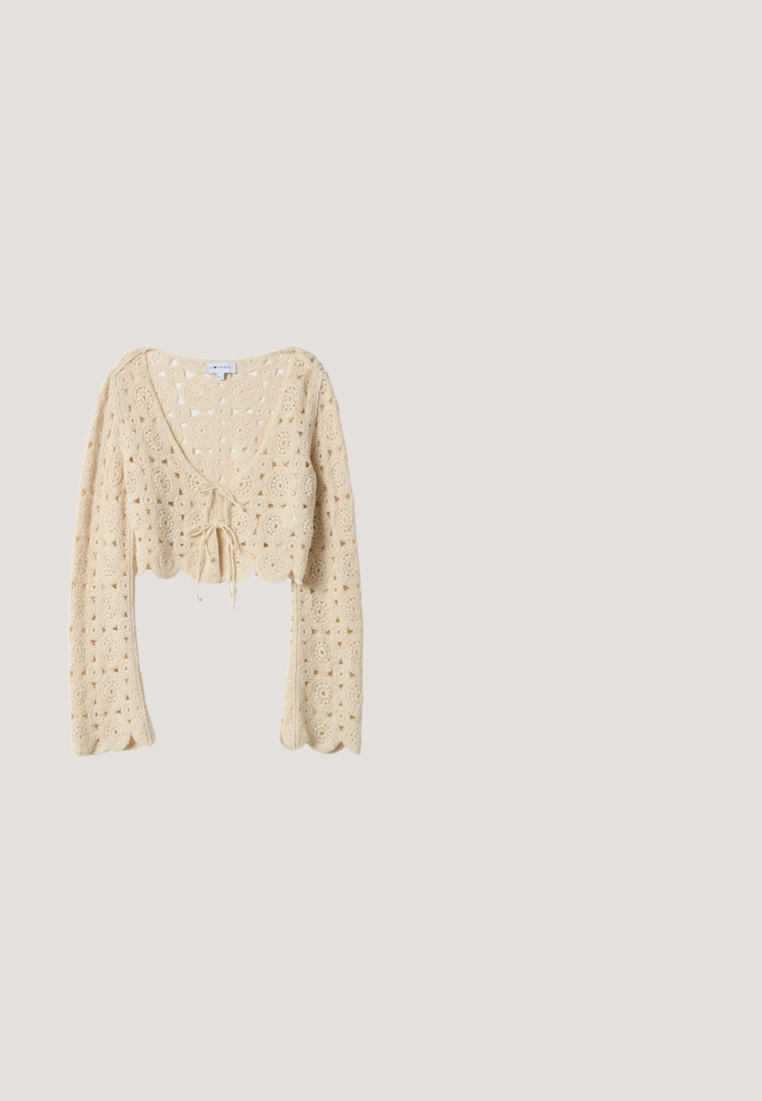 Cárdigan corto de punto crochet beige con mangas largas, bordes en forma de ondas y cierre de lazo en la parte delantera.; Vestido maxi floral con volantes sin mangas. Hecho de una tela ligera, con flores en tonos rosa y verde, una cintura con cordón y un dobladillo en capas.; Alpargata de cuña blanca con puntera cerrada, plataforma de yute trenzado y cintas para atar en el tobillo de tela beige y blanca tejida.; Bolso de paja beige tejido con ribete de cuero blanco y correa de hombro ajustable, exhibido sobre un fondo claro y liso.; Delicado collar de cadena de oro con un pequeño colgante en forma de trébol de cuatro hojas con borde dorado y centro blanco.; Cinturón tejido de paja beige con una hebilla circular trenzada, banda ancha y textura detallada, mostrado enrollado sobre un fondo blanco.