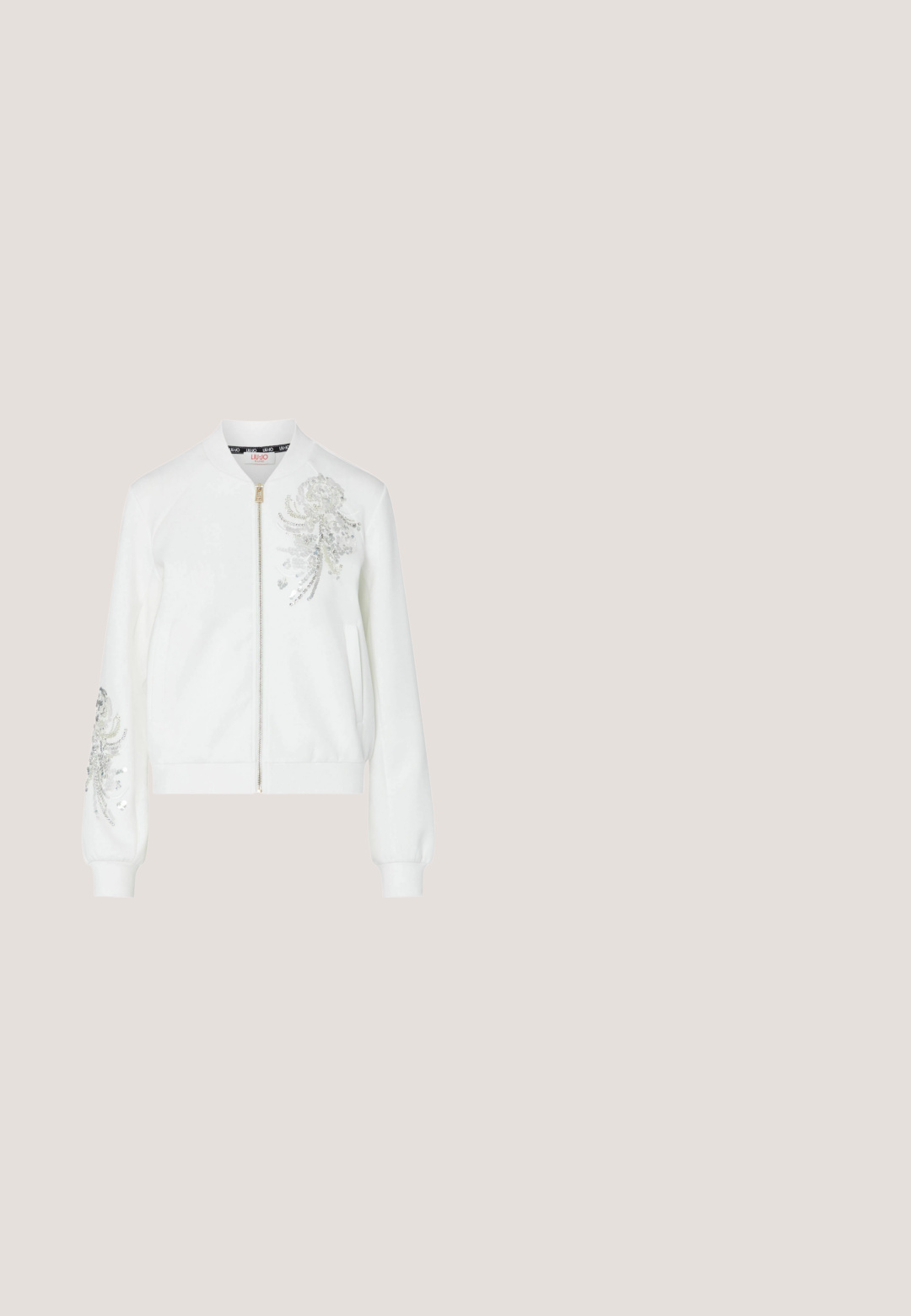 Veste blanche zippée avec ornements floraux en sequins argentés sur la poitrine et la manche gauche, dotée de poignets et d'une ceinture côtelés.; Crop top beige en tricot avec fines bretelles spaghetti formant un V dans le dos et un décolleté arrondi.; Short en jean blanc avec poches avant, fermeture par bouton et fermeture éclair, et clous argentés décoratifs sur la ceinture.; Baskets blanches avec un panneau brun texturé arborant un logo, des accents dorés, des lacets ronds et une semelle en caoutchouc. Silhouette athlétique classique.; Sac à main beige demi-lune avec une sangle noire, décoré de motifs floraux en strass argentés et transparents, avec une plaque logo Guess.; Bracelet en chaîne dorée avec des lettres en charme orthographiant "AMOUR," accents floraux, étiquette triangulaire et maillons décoratifs. Fermeture à cliquet à l'extrémité.