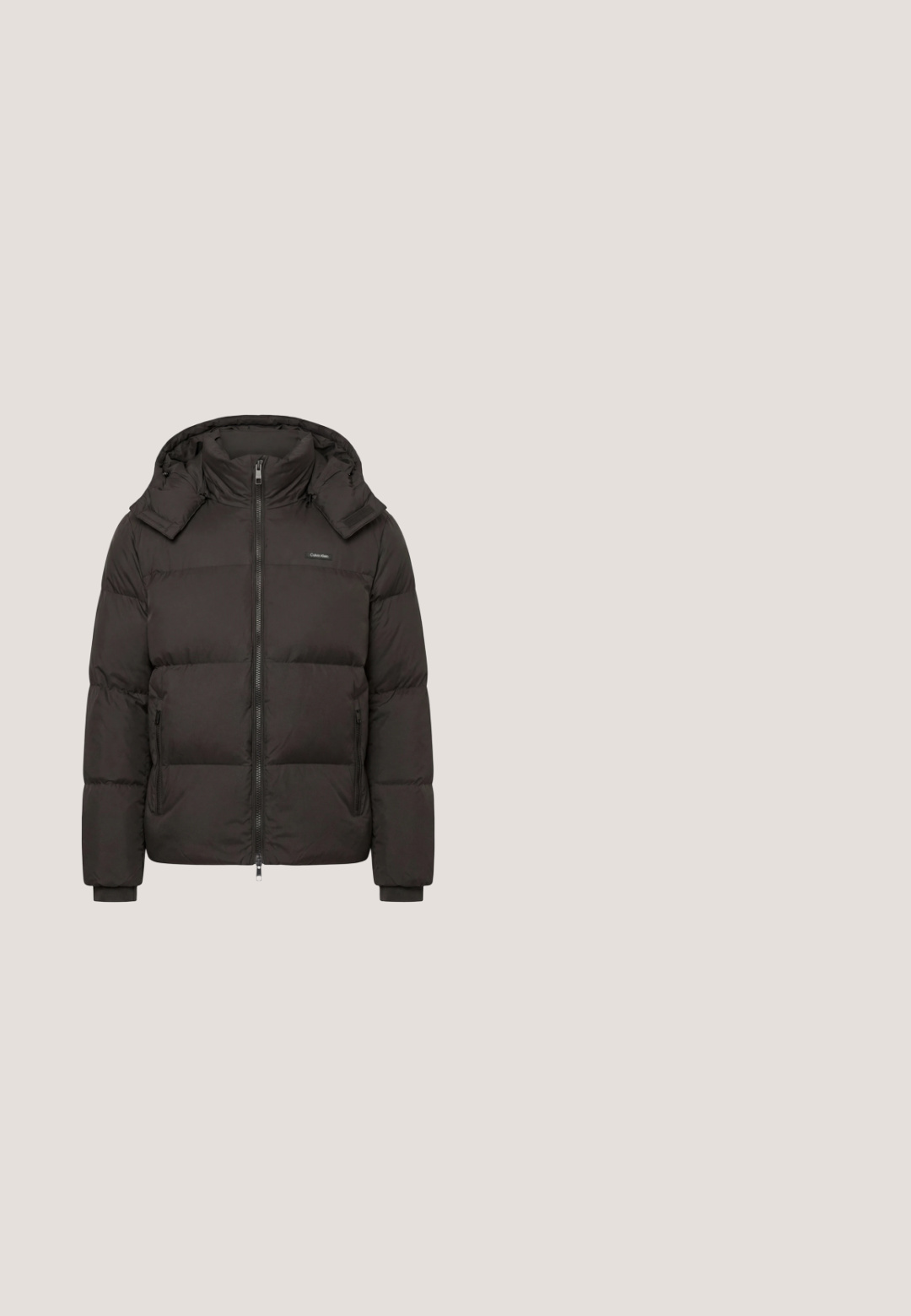 Zwart gewatteerd winterjack met rits aan de voorkant, hoge kraag, capuchon, twee ritssluitingen aan de zijkanten en manchetten bij de polsen.; Beige gebreide trui met een kraag met een kwart ritssluiting en lange mouwen, met een klein Calvin Klein-logo op de linkerborst.; Beige oversized T-shirt met korte mouwen, met "Calvin Klein" en een groot "cK" logo in wit en bruin geborduurd op de voorkant in het midden.; Donkerblauwe denim jeans met een recht model, vijf zakken en contrasterende stiksels op de naden. Gladde stofstructuur.; Beige suède enkellaarsjes met zwarte rubberen zool, vetersluiting en een klein logo dat aan de zijkant is gedrukt, voorzien van een trekloop aan de achterkant.; Bruine crossbodytas met zwarte riem, subtiel patroon, voorvak met rits en een klein rechthoekig merkembleem.