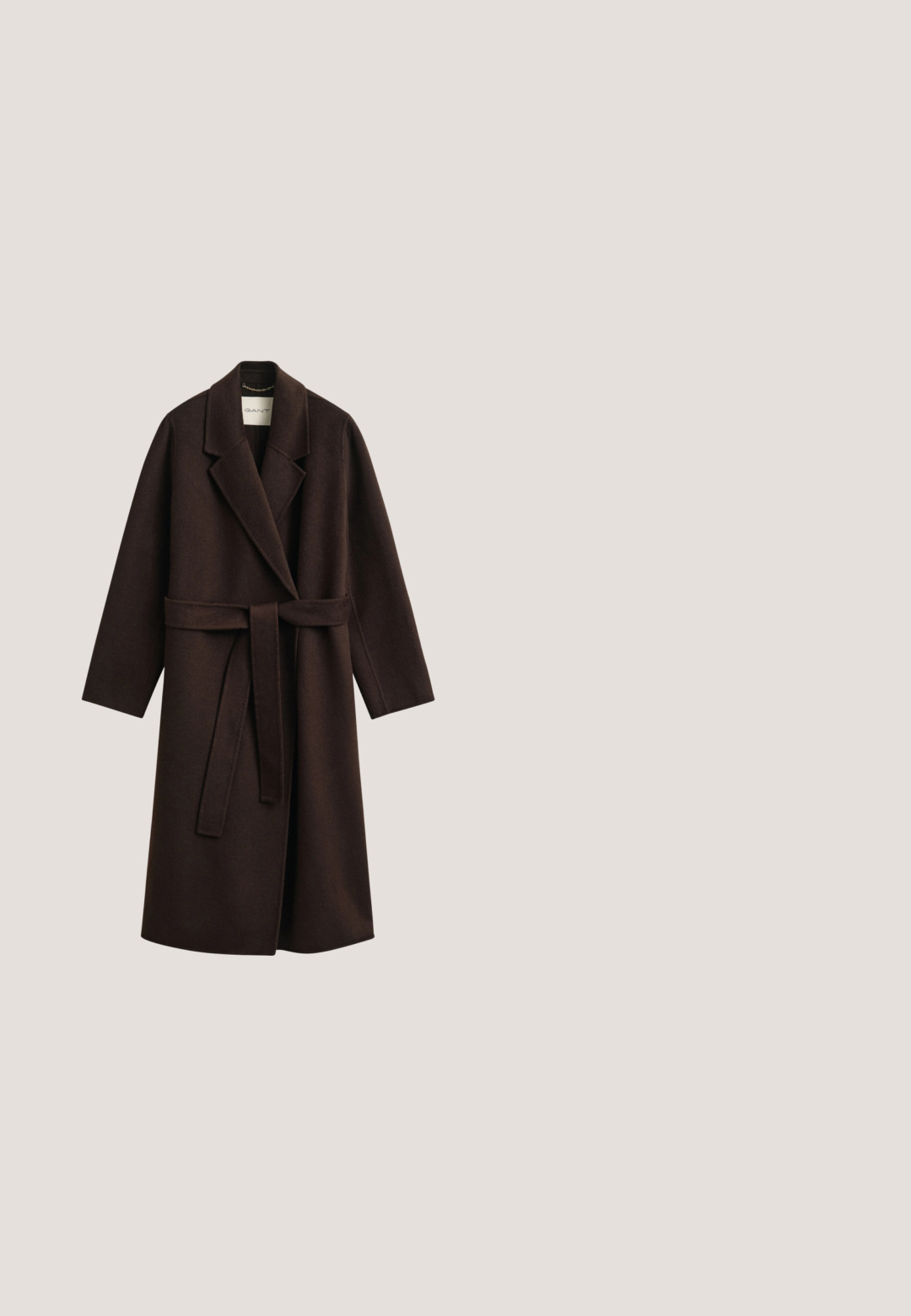 Long manteau en laine marron foncé avec ceinture, larges revers et manches longues, conçu pour temps froid.; Haut long à manches blanches en tricot côtelé avec un col rond et des fentes sur les côtés. Présente une texture lisse et une silhouette ajustée. Étiquette de la marque visible.; Pantalon large marron texturé avec taille élastique et jambes en forme de ballon resserrées aux chevilles sur fond blanc.; Chaussure plate en daim marron avec des détails en lacets et des œillets dorés, vue de côté sur un fond blanc.; Petit sac à main marron duveteux avec des poignées en cuir tressé sur un fond uni clair.; Collier chaîne en or avec de petites perles en pierre verte espacées uniformément sur un fond clair neutre.