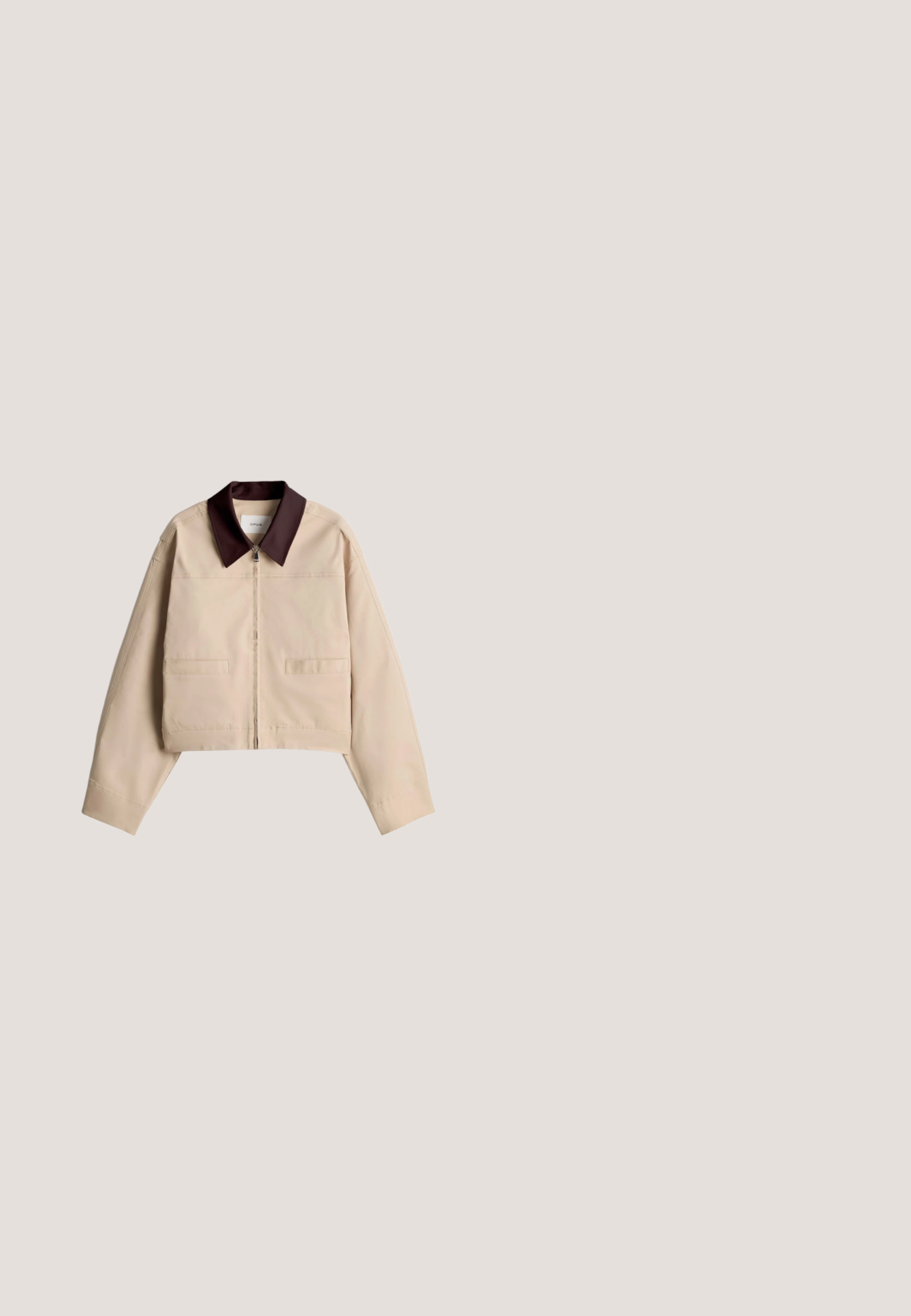 Beige kurze Jacke mit langen Ärmeln, Reißverschluss vorne, zwei Fronttaschen und kontrastierendem dunkelbraunem spitzem Kragen.; Dunkelolivgrünes Kurzarmtop mit schwarzen abstrakten geschwungenen Linienmustern und Rundhalsausschnitt.; Faltenrock in Dunkelgrün mit schwarzem Leopardenmuster. Elastischer Bund, leichtem Stoff und fließendem Design. Ausgestellte Silhouette.; Olivgrüner Mesh-Slipper mit einer strukturierten Oberseite, weißer Gummisohle und gerippten Akzenten entlang der unteren Kante.; Olivgrüne Ledertasche mit langen doppelten Griffen und dekorativem Quastenanhänger nahe der Griffbefestigung.; Armreif in Goldton in Bambusform mit glatten, facettierten Segmenten und der Gravur "ALLSAINTS" auf der Innenseite.
