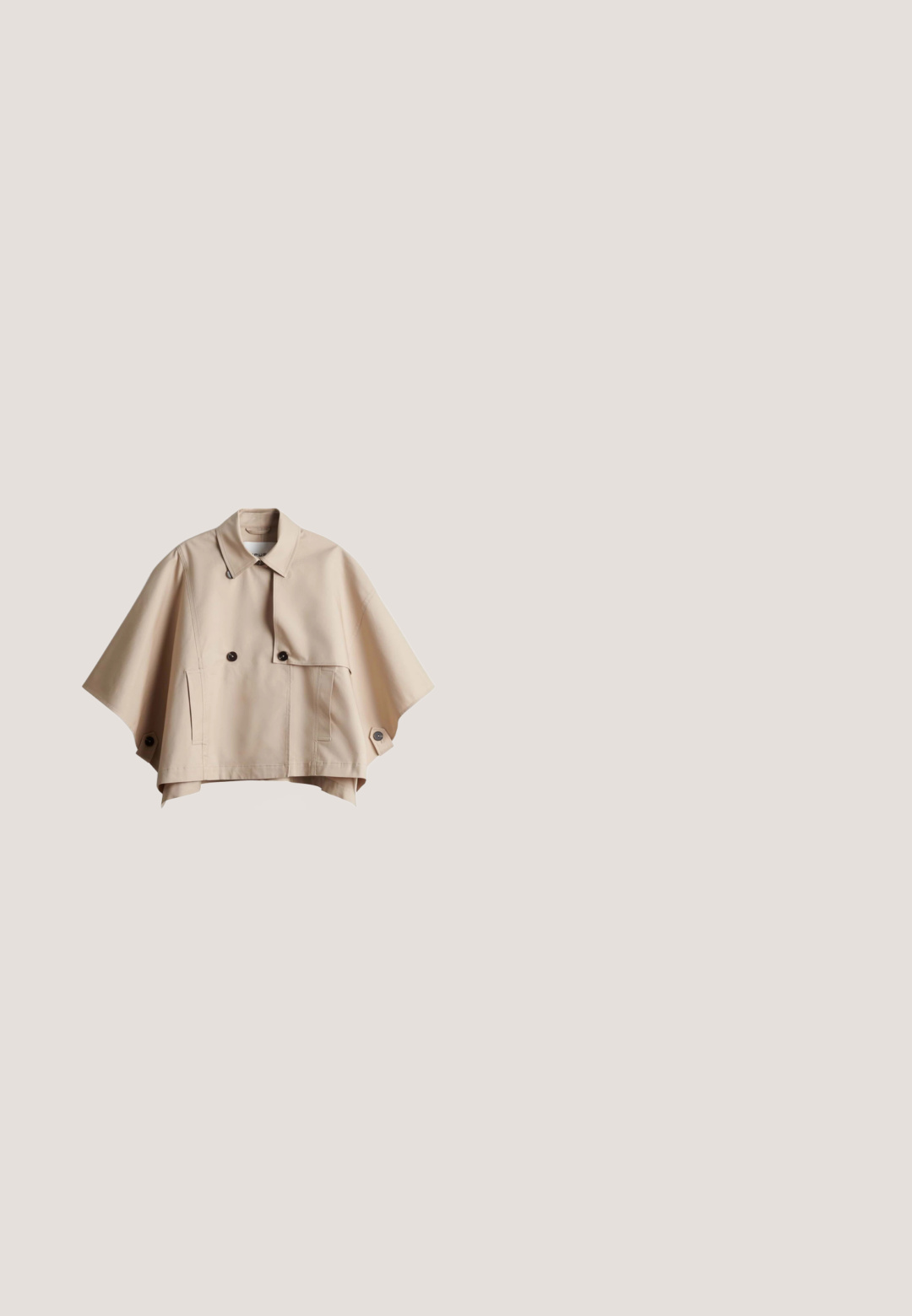 Beige cropped cape-style jas met brede mouwen, dubbelgeknoopte zwarte knopen, zijzakken en een kraag.; Olijfgroene jurk van textuurstof, met een kraag, korte mouwen en een losvallend ontwerp tot de enkels.; Wedges met espadrillezool, beige canvas gesloten teen, gevlochten jute zool, geweven hielstuk en verstelbare enkelband met metalen gesp.; Bruine transparante zonnebril met rechthoekige monturen en donkerbruine lenzen. De pootjes zijn voorzien van subtiele branding en hebben een gladde, glanzende afwerking.; Draagt tas met geweven beige body en olijfgroene leren riemen, handvatten en rand, voorzien van metalen studs en een ronde metal logo hanger.; Verstelbare gouden armband met groene en witte ronde kralen en kleine gouden zeshoekige kralen op een witte achtergrond.