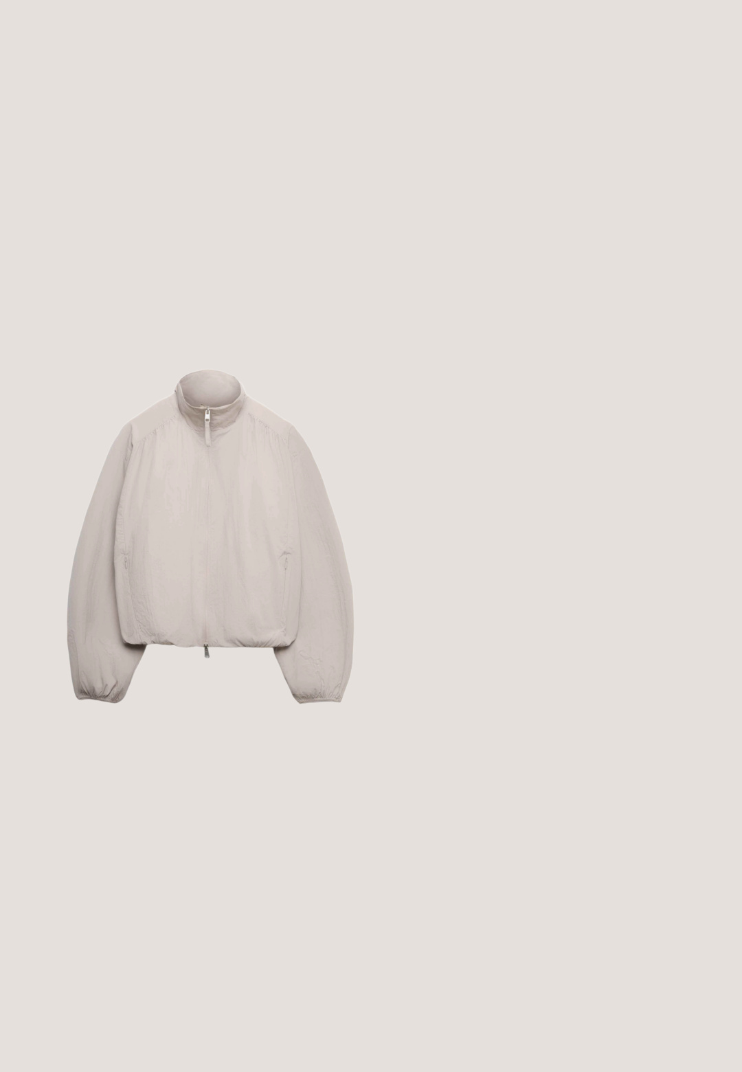 Lichtbeige jas met ritssluiting, hoge kraag, lange opgepofte mouwen, elastische boorden en elastische zoom, afgebeeld tegen een witte achtergrond.; Korte mouwen crew neck t-shirt van zachte lila stof. Beschikt over een eenvoudig ontwerp met strakke lijnen en minimalistische stiksels.; American Vintage ATUBAY - Shorts - arctique chine; Grijze suède sneaker met een wit leren accent, ronde neus, vetersluiting en groene hielstrook. Bevat contrasterende texturen en stikseldetails.; Lichtgrijze totebag met een gewatteerd ontwerp, dubbele handvaten en een voorvak. Heeft een gladde textuur en een minimalistische logodetail.; Zilveren slangketting armband met karabijnsluiting en een klein verlengkettingetje op een witte achtergrond.