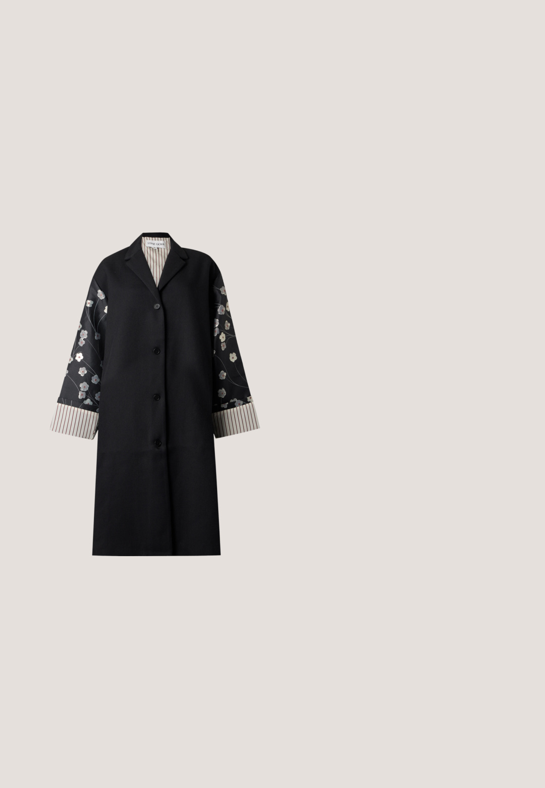 Abrigo largo negro con mangas estampadas con motivos florales, cierre frontal con botones y forro interior a rayas en puños y cuello de Stine Goya.; Hofmann Copenhagen EXCLUSIVE ALEXANDRA - Blusa - black; Falda larga de terciopelo negro adornada con un patrón de lentejuelas en forma de diamante, con una cinturilla suave y una silueta recta.; Botas negras de cuero hasta el tobillo con detalles de brogue, cordones en la parte delantera, cremalleras laterales y suelas de goma texturizadas. Combinadas con pantalones oscuros de corte slim.; Guantes de cuero negro con textura suave, con costuras a lo largo de los dedos y un diseño ajustado. Material suave y flexible para mayor comodidad.; Broche de oro ornamentado con cuatro formas de flores hechas de piedras preciosas facetadas azules, verdes y claras, dispuestas en un patrón simétrico.