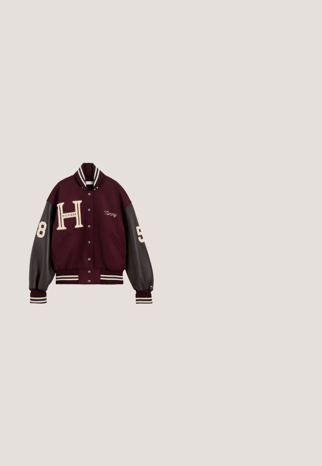 Vinrød og sort varsityjakke med trykknapper, store "H" og "Hilfiger" foran, "Tammy" broderet på brystet, og numrene 8 og 5 på ærmerne.; Marineblå T-shirt med korte ærmer med tynde hvide horisontale striber og et lille Tommy Hilfiger-logo midt på brystet.; Lyseblå lige ben jeans lavet af denim, med knaplukning, fem lommer og subtil falmning langs benene.; Brune lædersko med chunky sål, snørebånd og moc toe syninger, samt en tykk tan skridsikker platformsål, set fra siden på hvid baggrund.; Mørkerød læderhåndtaske med dobbelt håndtag, guldfarvet logo og tilhæftet koralfarvet læder lynlåspung.; Øreringe i sterling sølv med et snoet design, der har glatte og skinnende overflader. Ingen synlige mønstre eller aksenter.