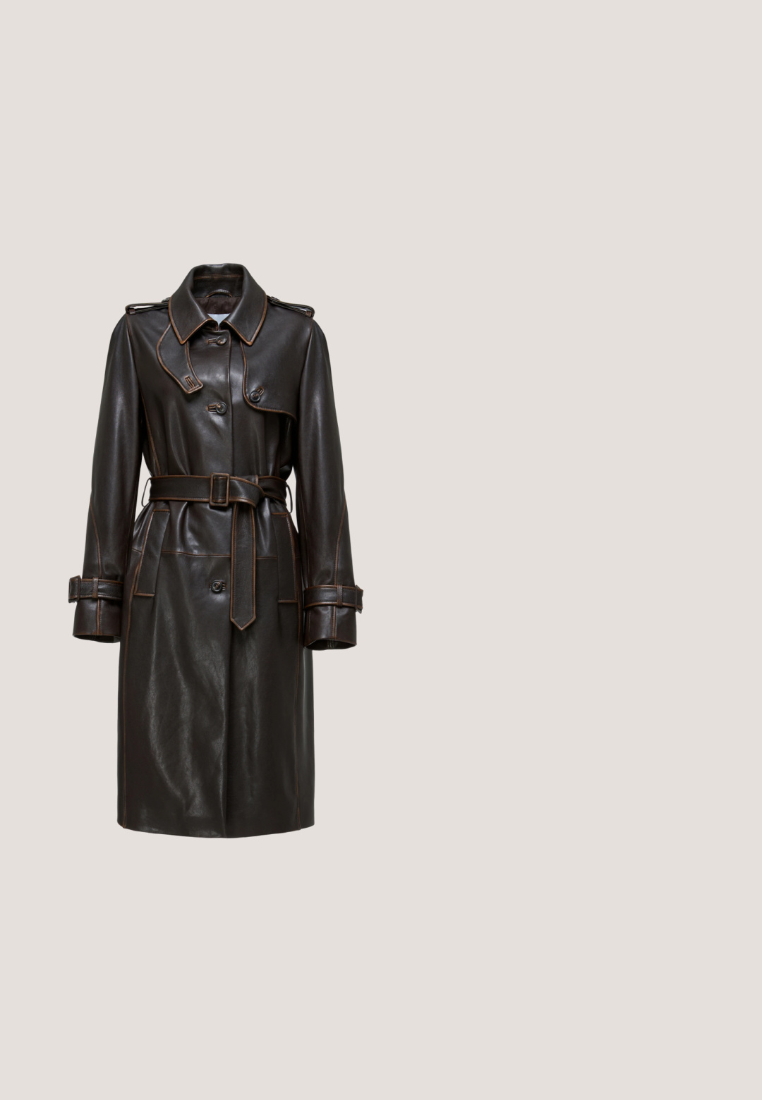 Bruine leren trenchcoat met een tailleband, dubbele knopen, grote kraag en contrasterende stiksels op de mouwen en details.; Donkerblauwe denim overhemd met lange mouwen, kraag met knopen aan de voorkant, twee borstzakken met kleppen en contrasterende gele stiksels.; Bruine, op maat gemaakte broek met een rechte pijp, gemaakt van gladde stof, voorzien van plooien en een standaard tailleband met lussen voor een riem.; Bruine suède cowboylaars met spitse neus, hoekige blokhak en lichtgekleurde decoratieve stiksels op schacht en voet.; Bruine leren totebag met ingewikkelde uitgesneden bloemenpatronen, gladde handvatten en een stevige basis voor stabiliteit.; Bruine leren riem opgerold met sierlijke antieke goudkleurige gesp, lus en uiteinde met bloemen- en geometrische gravures, op een witte achtergrond.