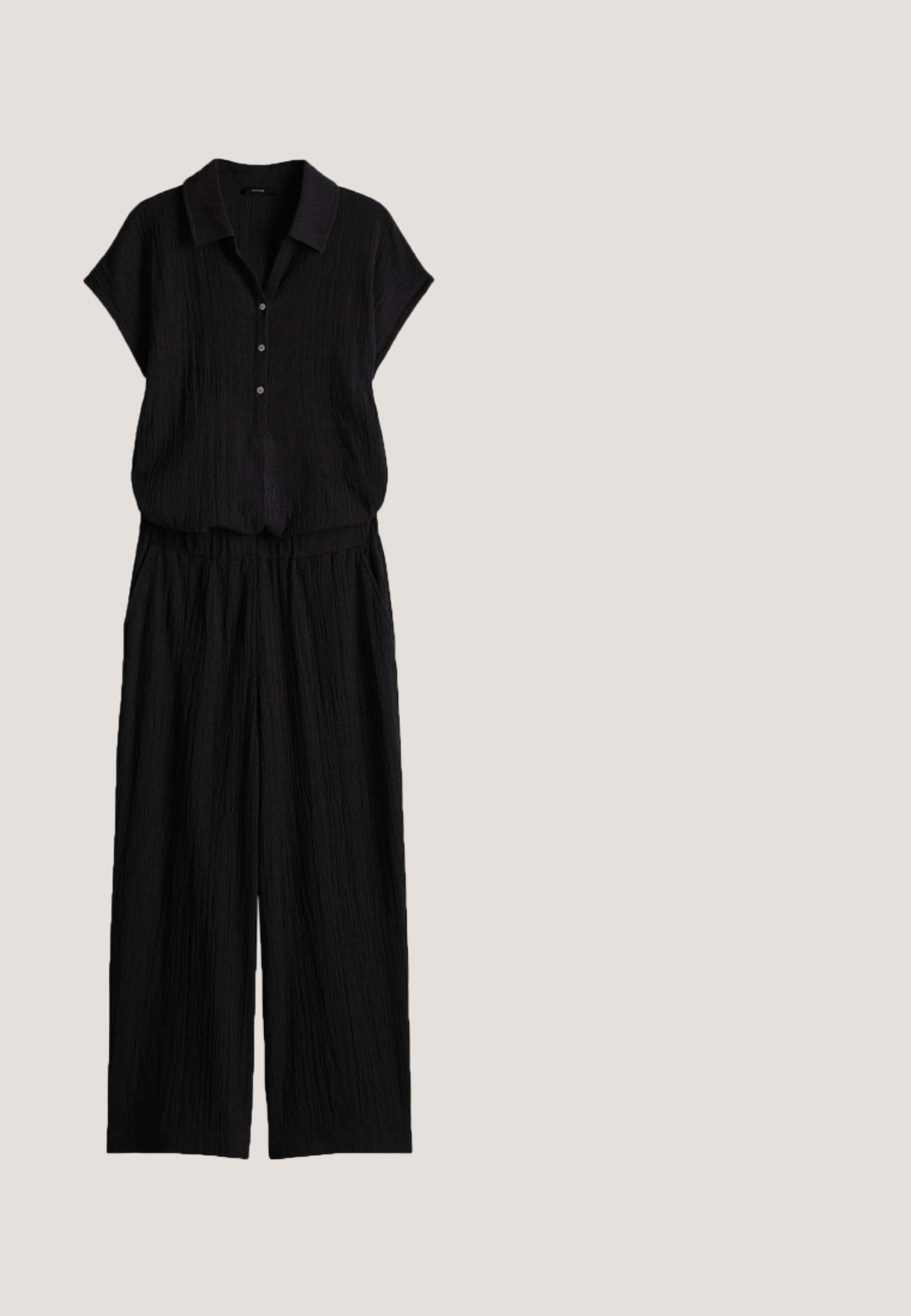 Zwart getextureerd tweedelig outfit met een kortemouwen coltop met knopen en wijde broek, gemaakt van lichte stof.; Zwart linnen mouwloos vest met een V-hals, voorzien van vijf knopen aan de voorkant, twee zakken vooraan en een gladde textuur.; Zwarte slide-sandalen met geweven stoffen banden en open teen. Voorzien van een dikke rubberen zool met textuurdetail en een gladde afwerking.; Zwarte zonnebril met hoekig cat-eye ontwerp, donker getinte lenzen, glanzende plastic montuur en subtiele gouden accenten op de pootjes.; Zwarte geweven draagtas met halfcirkelvormige gouden metalen handgrepen op een witte achtergrond.; Zwart verstelbaar touwarmbandje met een metalen sluiting in goudkleur en een ronde hanger gegraveerd met "CPH STUDIOS."