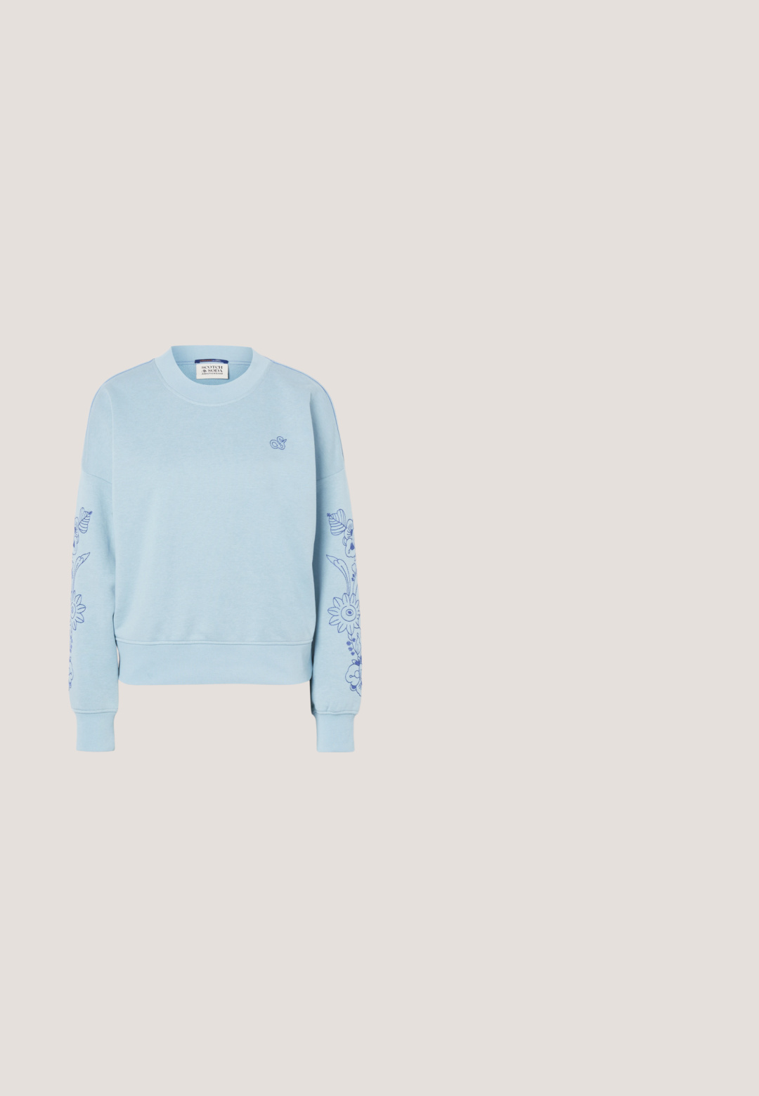 Lyseblå sweatshirt med rund halsudskæring, blomsterbroderi på begge ærmer og et lille broderet logo på venstre bryst.; Lyseblå t-shirt med korte ærmer og rund hals med lille broderet logo på venstre bryst og GANT-mærke indeni kraven.; Lyseblå denimjeans med lige ben, høj talje, fem lommer, knaplukning og diskret falmning i stoffet.; Hvid læder- og mesh-sneaker med snørebånd svævende over beige tæppe, rundt træbord med bøger og lysefarvet sofa i baggrunden.; Grå ruskind tote taske med to mørke læderhåndtag. Har stikninger på siderne, blød tekstur og en rummelig åbning.; Sølv hoop ørestik med en poleret overflade, prydet med små guld accenter og en rund form, båret på øreflippen.