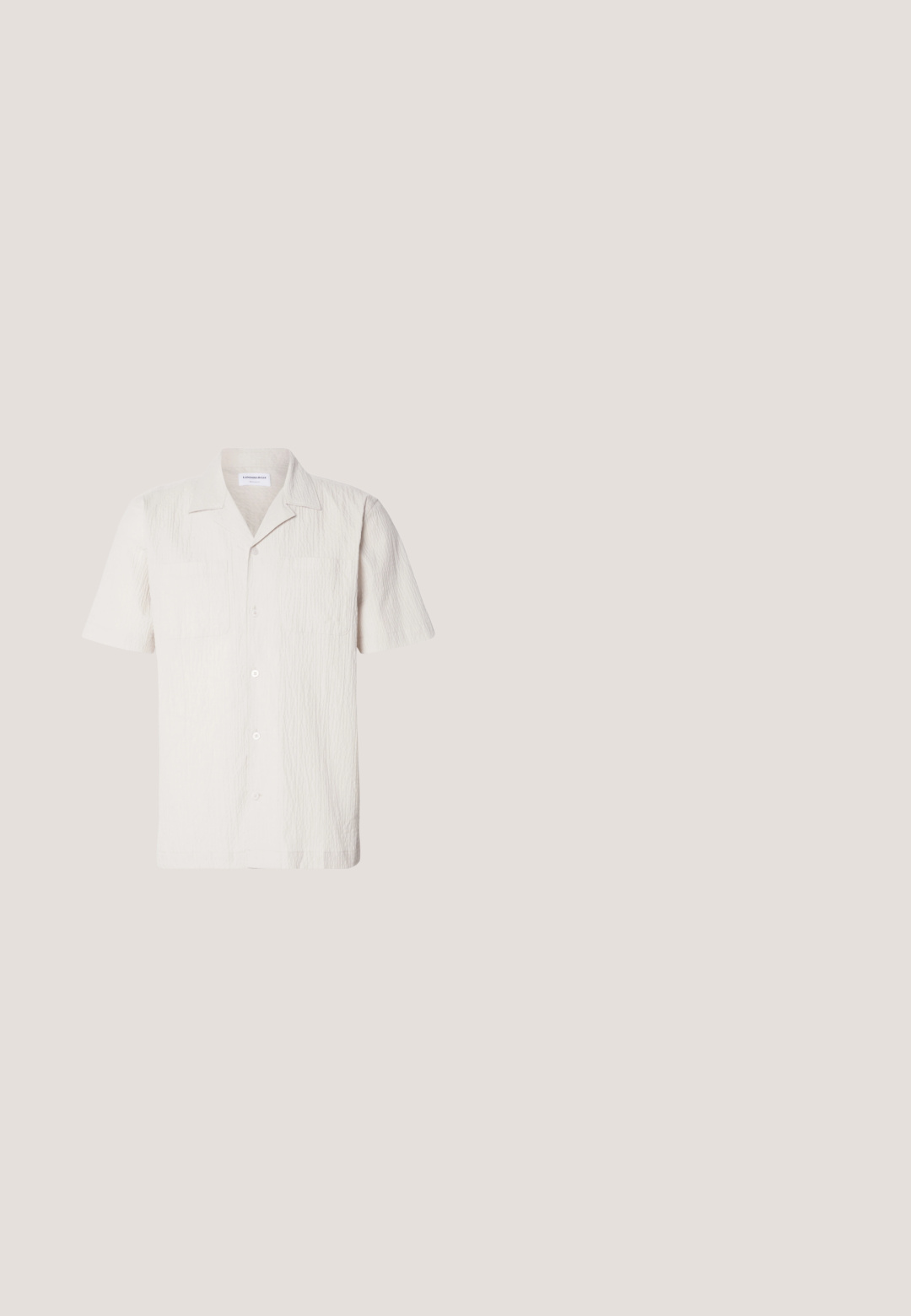 Chemise à manches courtes, de couleur beige clair, en tissu texturé, avec un col encadré et deux poches poitrine, dotée d'une fermeture frontale à boutons.; Shorts beiges en tissu léger, avec un devant plat, des poches latérales et une fermeture à un bouton à la taille.; Sandales en cuir marron avec un design à lanières, ornées d'un détail de boucle, portées avec un pantalon vert sur une surface texturée.; Lunettes de soleil en écaille de tortue avec des verres verts, présentant une forme octogonale et des branches minces et courbées. Le matériau a une finition brillante.; Sac fourre-tout en toile crème avec poche avant, deux poignées, bandoulière réglable et petit texte jaune "O.N.S" en bas à droite de la poche.; Ceinture en cuir tressé marron avec une boucle en argent. Elle présente une texture tissée et un accent en cuir lisse près de la boucle.