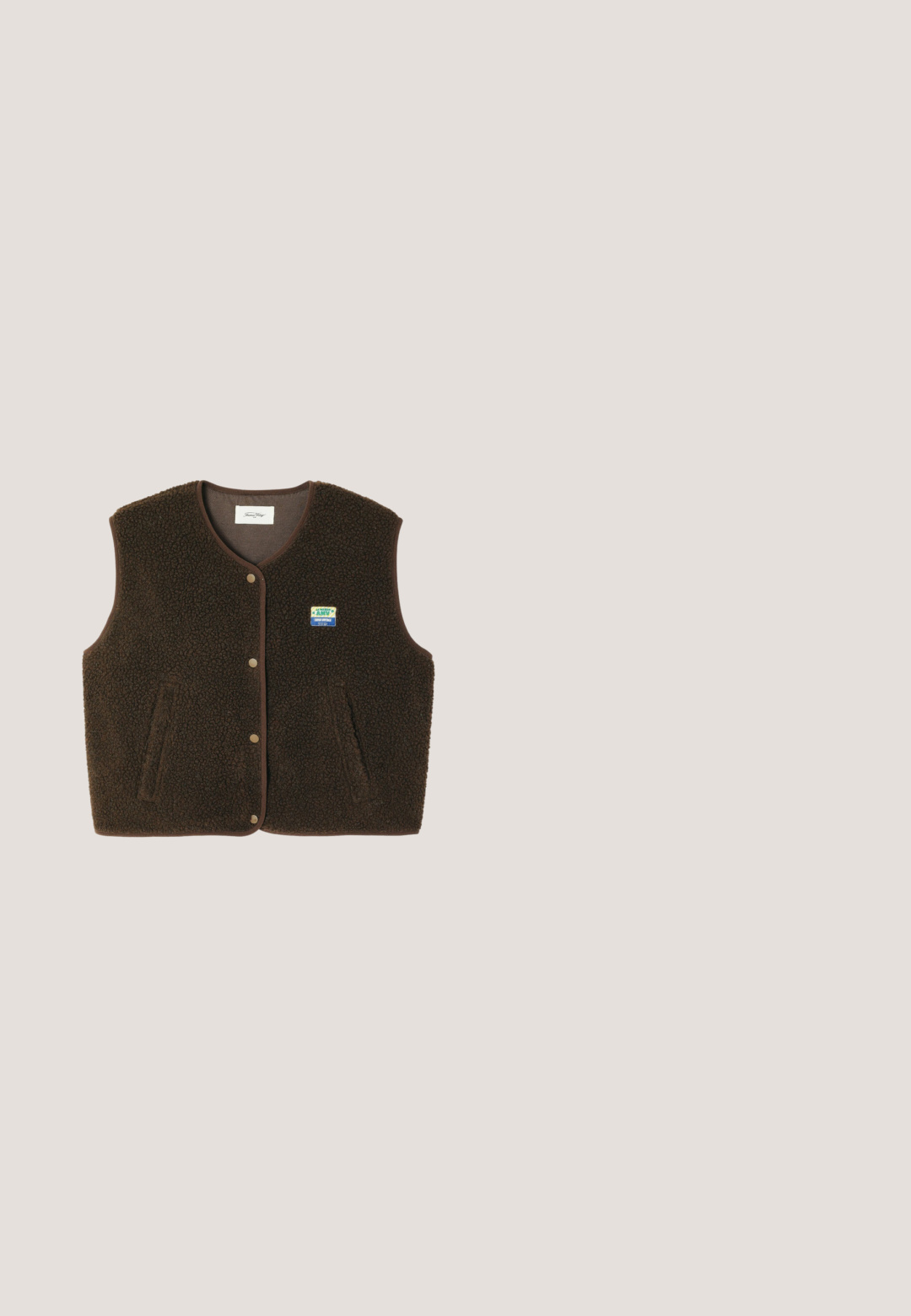 Bruine mouwloze fleecebodywarmer met drukknoopsluiting aan de voorkant, twee zijzakken en een kleine rechthoekige blauw-gele patch op de linkerborst.; Bruin katoenen t-shirt met korte mouwen, klein geborduurd logo op de linkerborst en een ronde hals.; Bruine wijde jeanstype met een textuurpatroon, voorzien van een ritssluiting en knoop, zilverkleurige hardware en contrasterende donkere accenten.; Bruine leren platform sneakers met een gestructureerde bovenkant, witte stiksels, vetersluiting en gele accent op de rand van de zool.; Bruine oversized omringende zonnebril met licht amberkleurige getinte glazen en dik montuur, gezien van voren op een witte achtergrond.; Camouflagepatroon Vans crossbody tas met voorvak met ritssluiting, zwarte verstelbare schouderriem en klein bovenhandvat.
