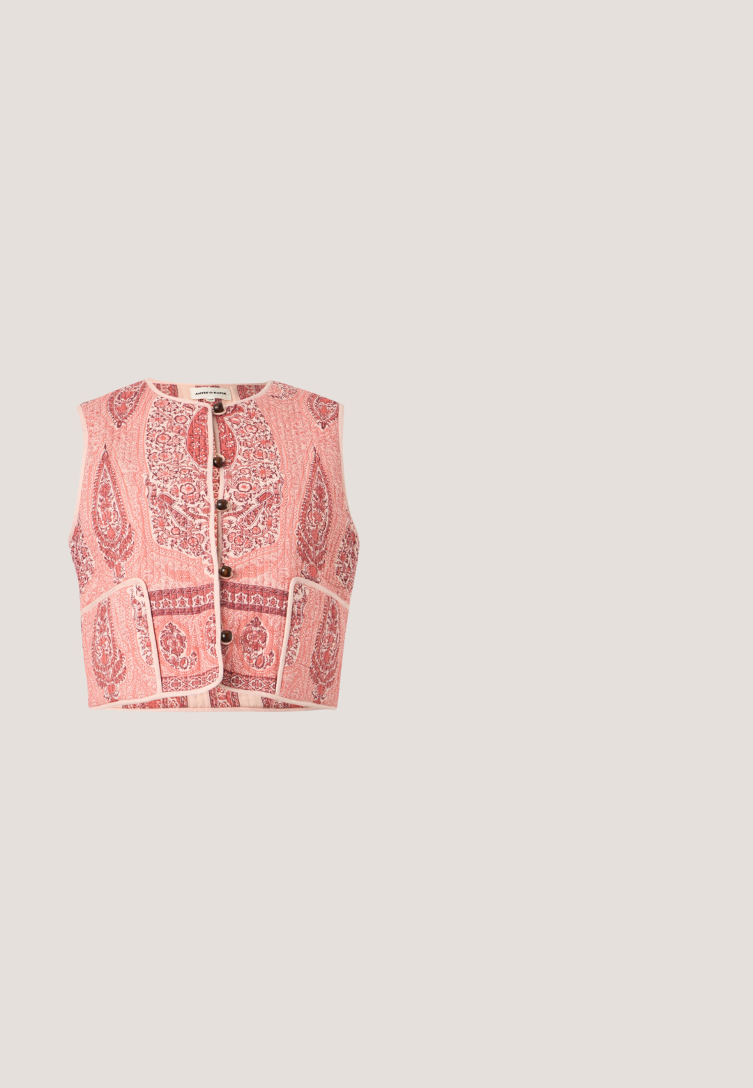 Chaleco acolchado sin mangas de color rosa con intricados patrones florales y de cachemira, botones de madera en la parte delantera y dos bolsillos frontales.; Camisa blanca de manga larga con un escote rojo con forma de ondas. Presenta un pequeño bordado de una fresa verde y roja en el frontal.; Pantalones con cintura elástica rosa claro, piernas anchas y bajos ondulados bordados con pequeños ojales.; Mules de cuero rojo con punta puntiaguda y tacón bajo, con detalles recortados en los laterales y textura suave. Diseño elegante y aerodinámico.; Bolso de cuero rosa tejido con un asa corta dorada y una correa larga desmontable sobre un fondo blanco liso.; Par de pendientes de flor en tono dorado con pétalos de esmalte rojo y un centro de piedra preciosa cuadrada amarilla sobre un fondo blanco.