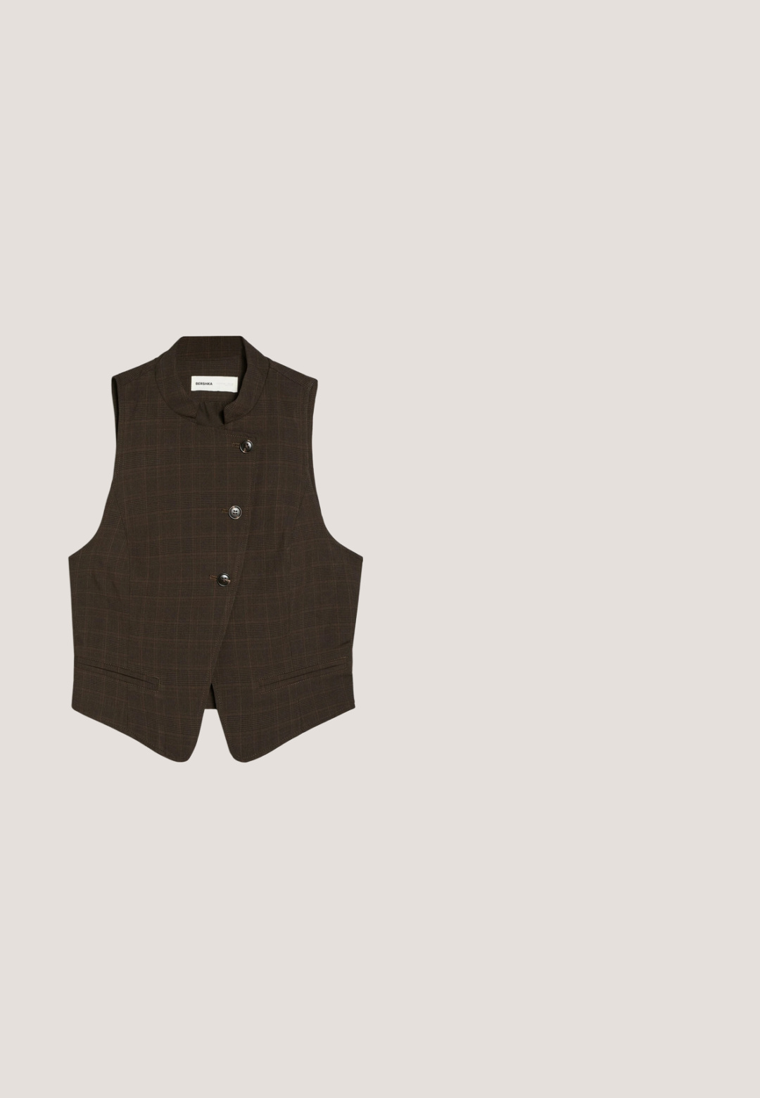 Donkerbruine mouwloze vest met hoge kraag en drie knopen aan de voorkant, met een subtiel geruit patroon en twee voorzakken.; Beige poloshirt met bruine horizontale strepen, donkerbruine kraag en knopenlijst, en een klein logo op de linkerborst.; Donkerbruine broek met wijde pijpen, hoge taille en dubbele zilveren gespen aan de riemen, voorplooien en zijzakken.; Bruine suède schoenen met een ronde neus en een tan rubberen zool, voorzien van een simpel vetersysteem, gecombineerd met lichtblauwe denim broek.;  Schildpadbril met een vierkant montuur, voorzien van heldere lenzen en een gestructureerd patroon. De pootjes hebben een dunne, gestroomlijnde vorm.; Bruine leren crossbodytas met witte stiksels, rechthoekige vorm en verstelbare riem met gesp.