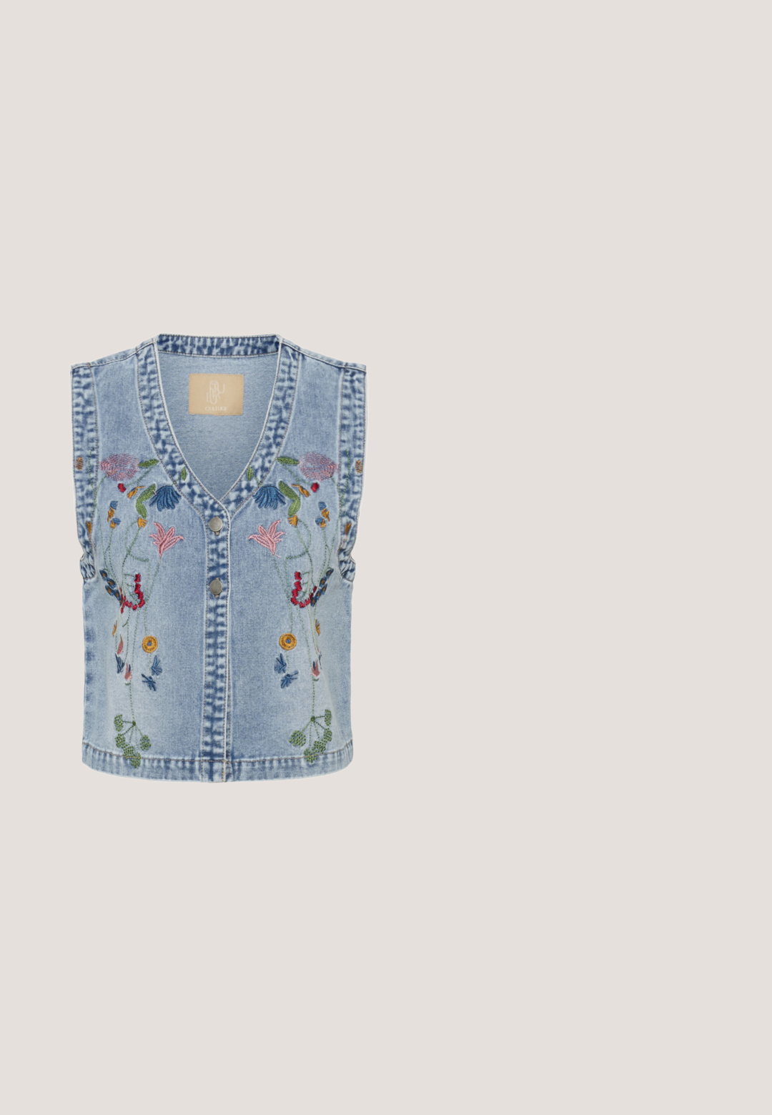 Lichtblauw denimvest met V-hals, knopen aan de voorkant en kleurrijke bloemenborduursels langs de schouders en het midden voor.; Lichtblauwe blouse met gegolfde randen en fluttermouwen. Heeft oogjesborduurwerk en een drieknoopsluiting bij de V-hals.; Blauw-witte gestreepte shorts met witte geborduurde bloemenkant, elastische tailleband en gerimpelde zoom.; Slip-on espadrille met blauw-witte strepen en geborduurde citrusfruithoezen op de neus, met een gevlochten jutezool.; Octagonale zonnebril met dunne gouden metalen monturen en bruine gradiëntlenzen, geplaatst op een witte achtergrond.; Rechthoekige witte handtas met lichtblauwe bloemembroidery, franjes en twee verstelbare witte banden.