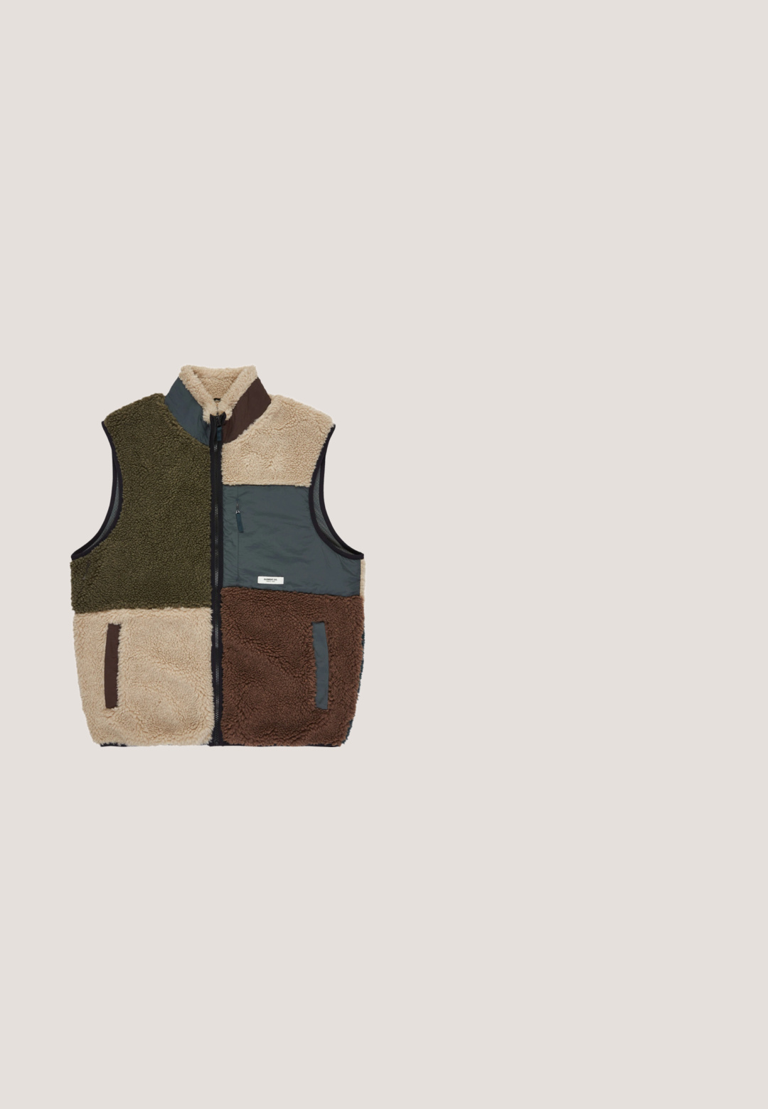 Fleece vest met hoge kraag, voorzien van groene, beige, grijze en bruine panelen. Ritszak aan de voorkant, textuurstof over de hele vest.; Oliijfgroene Vans hoodie met voorzak (kangoeroezak), capuchon met koordje, geribde boorden en klein Vans-logo op de borst.; Beige katoenen T-shirt met korte mouwen, een ronde hals en een klein wit logo op de borst. Soepele textuur met een ontspannen pasvorm.; Vans MN RANGE RELAXED ELASTIC - Broek - dried kelp; Groene suède sneakers met een witte rubberen zool, vetersluiting, gevoerd kraag en het DC-logo aan de zijkant.; Groene schoudertas van duurzaam materiaal, voorzien van een voorste ritszak, een zwarte strap en een horizontale witte accentstrap.