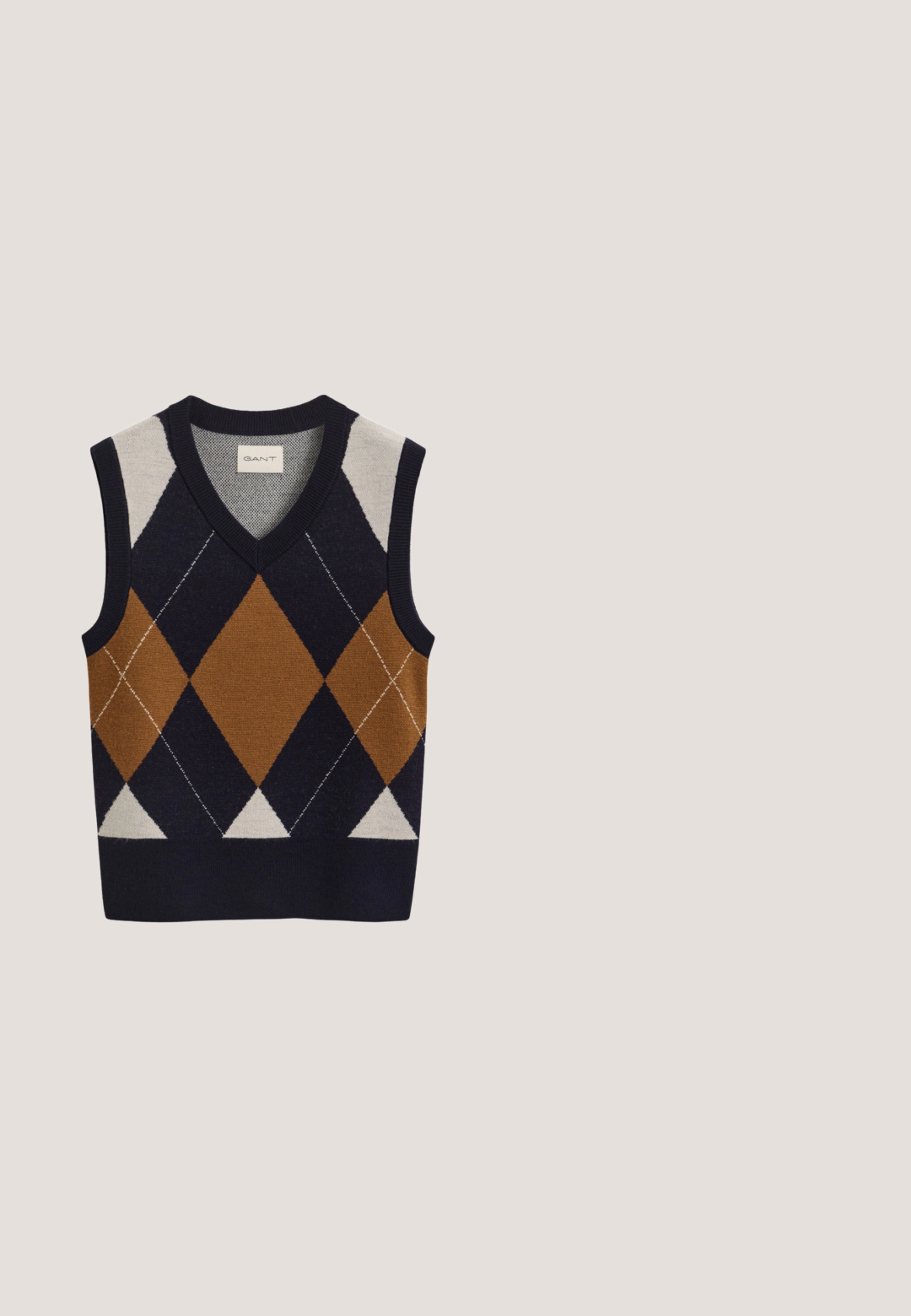 Mouwloze gebreide vest met V-hals, met een groot bruin, marineblauw en crème argyle-patroon aan de voorkant.; Marineblauw tweed jasje met gouden knopen, rode en witte biezen, twee voorzakken en een kraag met rafelige randen. Getailleerde pasvorm met lange mouwen.; Wit overhemd met lange mouwen, kraag, knoopmanchetten en een subtiel logo op de linkerborst.; Bruine en witte geplooide rok met een gestructureerd ontwerp en een frisse textuur, met een hoge taille en meerdere verticale plooien.; Donkerbruine gepolijste leren heren penny loafer met lage hak en gestikte details op witte achtergrond.; Bruine leren handtas met bovenhandvat, voorflapsluiting en gouden ovale logoplaat met de tekst "The Bridge."