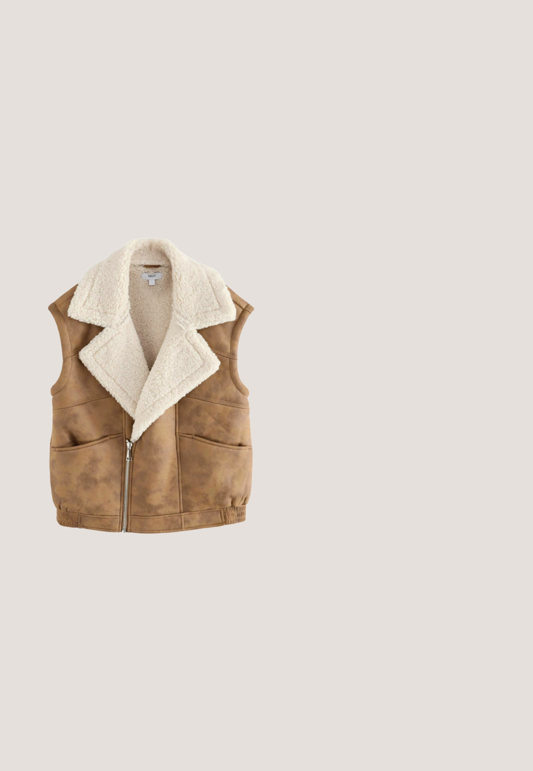 Bruine mouwloze vest met een pluche crèmekleurige kraag, ritssluiting en twee voorszakken. Gemaakt van textuur faux leer.; Crème ribbelgebreide top met korte mouwen, een ronde halslijn en een getailleerde pasvorm, die een zachte textuur en lichtgewicht materiaal toont.; Beige slim-fit enkellange broek met een gladde afwerking en zonder zichtbare zakken of versieringen op een effen achtergrond.; Bruine leren knielange laars met twee gouden gespen, lage zwarte blokhak en een treklipje aan de achterkant op een witte achtergrond.; Kleine beige leren crossbodytas met zilverkleurige gesp en afneembare verstelbare band op witte achtergrond.; Bruine suède riem met een gegraveerde gesp van metaal in goudkleur, opgerold op een effen lichte achtergrond.