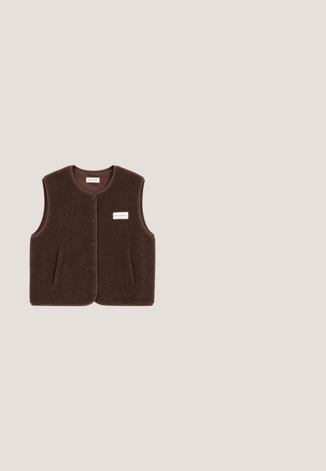 Brun ærmeløs fleecevest med knapper foran, to sidelommer og en lille rektangulær "OH APRIL" label på brystet.; Brun strikket sweater med høj hals og brede ærmer, med teksten "GOOD KARMA CLUB" i lyseblå over forsiden.; Brune bukser med vide ben, elastisk talje og snøre foran, lavet af blødt strikstof.; Brune ruskinds ankelstøvler med faux pelsfor, rund tå og en tykk platformsål; har en syet søm og en trækflap bagpå.; Rektangulære skildpaddemønstrede solbriller med mørkebrune linser og slanke arme, vist mod en hvid baggrund.; Brun struktureret tote taske med to skulderremme og sidelommer, vist på en hvid baggrund.