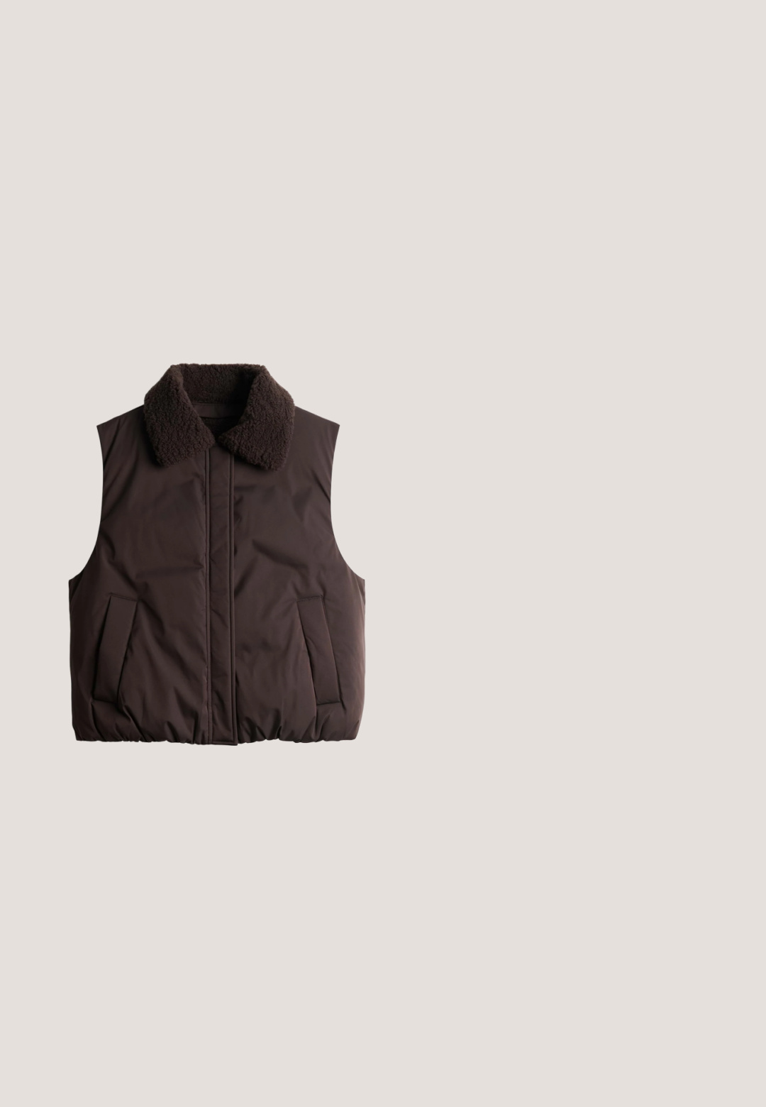 Veste sans manches matelassée marron foncé avec col épais texturé et poches avant, posée à plat sur un fond blanc.; Sweatshirt marron avec des rayures verticales blanches, présentant un col rond, des épaules tombantes et un ourlet légèrement court. Matière en mélange de coton.; Chemise marron à manches longues avec col roulé, coupe ajustée, texture lisse, sans motifs ni ornements visibles.; Pantalon marron à jambes larges avec une texture côtelée, doté d'une taille haute sans quincaillerie ni motifs visibles. Tissu lisse et fluide.; Chaussures en daim marron sans lacets avec un bout rond, un profil bas et une semelle en caoutchouc texturée. Présentent un design simple et épuré.; Grand sac fourre-tout en daim marron avec deux longues bandoulières et un simple détail de couture verticale sur le devant, présenté sur fond blanc.