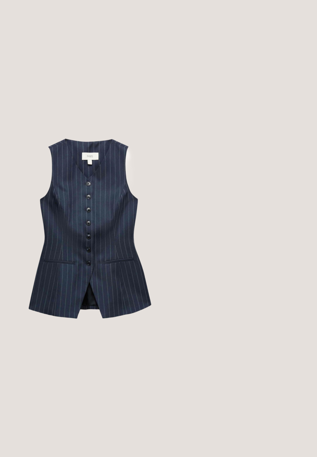 Marineblauw damesmouwloos gilet met krijtstreep, zes zwarte knopen aan de voorkant en twee voorzakken met rand.; Witte shirt met puntkraag, lange mouwen, knopen aan de voorkant, een enkele borstzak, gebogen zoom, gemaakt van een gladde stof. Subtiele logodetail.; Marineblauwe broek met krijtstrepen en een rechte pijp. Voorzien van een tailleband en zijzakken. Gemaakt van een gladde stof met een subtiele textuur.; Donkergroene suède slingback schoen met spits toelopende neus en lage uitlopende metalen hak met verstelbare gespband.; Donkerblauwe leren handtas met dubbele ronde handvatten, goudkleurige hardware en een afneembare schouderband. Beschikt over een gestructureerd oppervlak en een logo-detail.; Delicaat armbandje met kleine donkerblauwe kraaltjes en gouden ronde tussenstukjes, met een gouden karabijnsluiting en een verstelbare ketting met bedel.