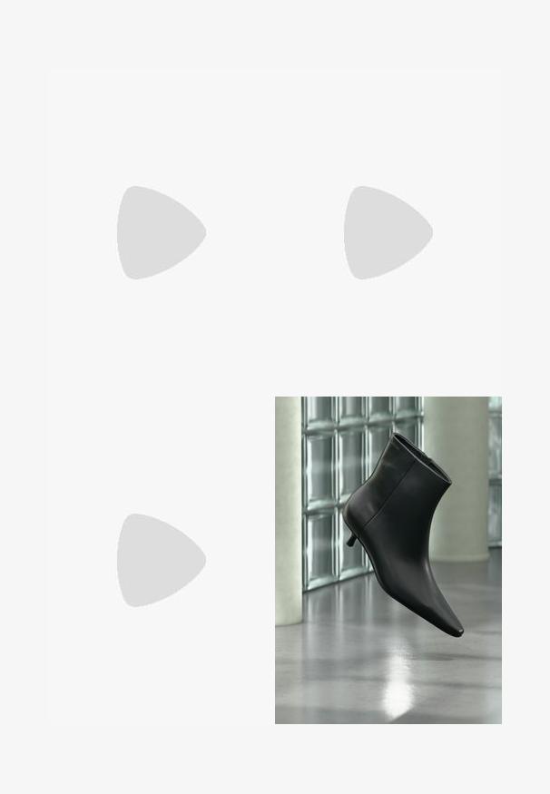 Mono negro con cremallera frontal, diseño sin mangas, cuello alto y piernas anchas. Tela suave y texturizada con sutiles detalles de costura.; Botín negro de cuero con punta puntiaguda y tacón bajo estilo kitten, mostrado en ángulo sobre un suelo pulido y con una pared de bloques de vidrio de fondo.; Bolso de hombro negro de cuero con textura de cocodrilo, con correas largas y un pequeño colgante de logo plateado en una correa.; Calvin Klein SPIRAL - Pulsera - silver-coloured