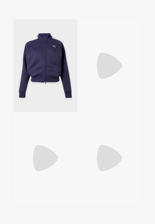 Veste de survêtement Puma bleu marine à fermeture éclair, avec bandes blanches sur les épaules, col montant, poches avant, poignets et ourlet côtelés, présentée sur fond uni.; T-shirt noir oversize à manches courtes, avec un grand logo Puma blanc au centre devant.; Jupe courte sportive noire avec taille élastique, liseré blanc sur le côté et petit logo Puma sur le côté inférieur droit.; Chaussure plate Puma rose et blanche avec des lacets reposant sur une marche en béton gris à l'extérieur.