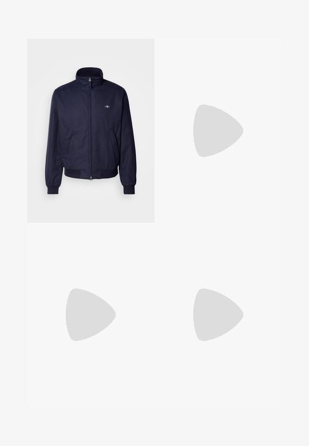 Marineblauwe bomberjack van gladde stof, met een opstaande kraag, voorrits, elastische manchetten en zijzakken. Subtiele logodetail aanwezig.; Marineblauw katoenen T-shirt met een witte opdruk van "GANT SPORTSWEAR," "NEW HAVEN," en "1949." Ronde halslijn en korte mouwen.; Donkerblauwe denim jeans met een recht pijpdesign, contrasterende stiksels, een knopenrits en vijf-pocketstijl.; Beige sneakers met een textuur op de mesh neus, een bovenwerk van glad leer en contrasterende logo-accenten. Platte rubberen zool met een strak ontwerp.