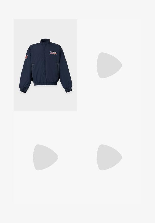 Marineblauwe racejas met rits met Oracle Red Bull Racing-logo op de borst en een Red Bull-patch op de linkermouw.; Rood T-shirt met korte mouwen en ronde hals, met wit "Red Bull Racing" logo op de linkerborst.; Grijze sweatpants van een zachte katoenmix, met een elastische tailleband, recht model en een klein logo aan de linkerkant.; Lichtgrijze Nike sneaker zweeft boven ruwe betonnen trappen met schaduwen die de contouren en textuur versterken.