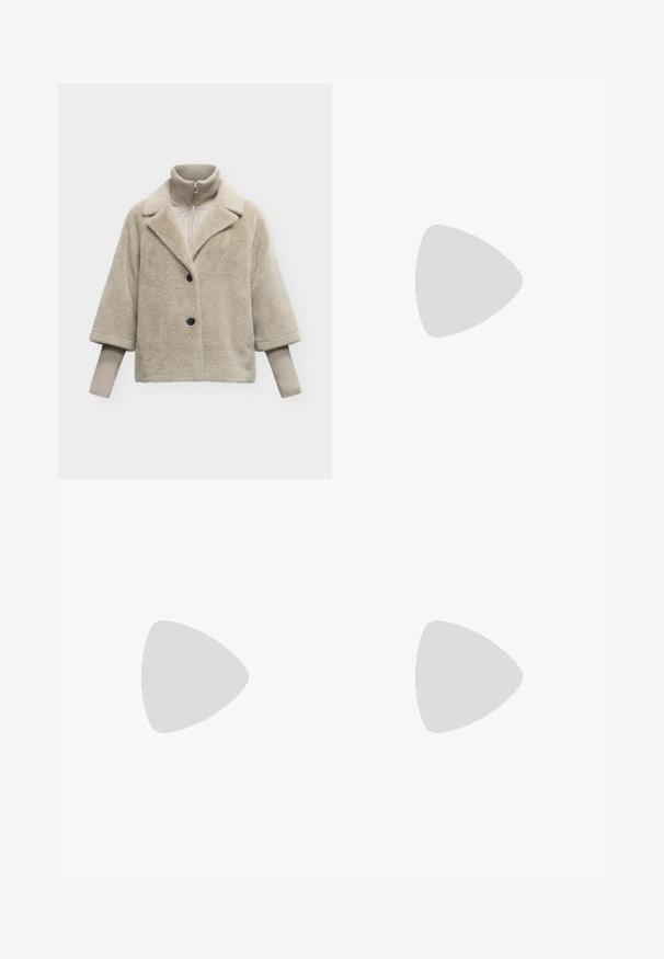 Manteau en fausse fourrure beige avec deux boutons noirs sur un pull beige côtelé à col montant avec fermeture éclair et manches longues.; Haut à manches courtes rayé en bleu clair et marine, avec un décolleté en V et un tissu doux et texturé avec des rayures horizontales.; Pantalons larges noirs à taille haute, avec des détails de boutons à la taille et des plis sur le devant.; Femme aux longs cheveux noirs appuyée sur une chaise blanche courbée, portant un chemisier taupe, un pantalon beige, une ceinture noire et des bottines noires à talons.