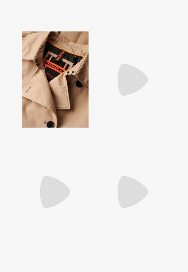 Beige trenchcoat met donkere knopen, dubbele borstsluiting en zwarte kraagvoering. Voorzien van een "SUPERDRY" label in oranje en zwart.; Effen wit T-shirt met korte mouwen en ronde hals, met een rechte zoom, gepresenteerd tegen een witte achtergrond.; Zwarte wijde broek met riemlussen, knoop aan de voorkant en rits, plat neergelegd op een witte achtergrond.; Zwarte Adidas sneaker met witte strepen en gumzool die boven grijze betonnen trappen zweeft in natuurlijk licht.