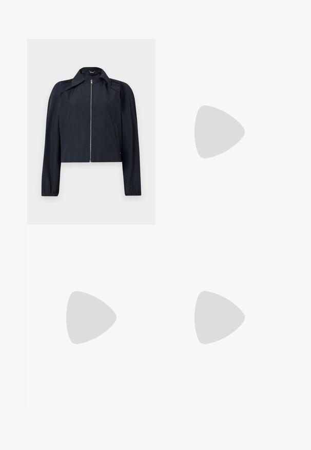 Veste légère bleu marine avec fermeture éclair frontale, manches longues, col et poches latérales sur un fond clair uni.; Blouse gris clair à manches courtes avec col montant et fentes sur les côtés, confectionnée dans un tissu doux et fluide avec un ourlet arrière légèrement plus long.; Pantalon crème à taille haute et jambes larges avec plis devant, fermeture éclair avant dissimulée et passants pour ceinture.; Bottine en cuir noir à bout pointu et petit talon kitten, présentée en angle devant un sol poli et un mur en blocs de verre.