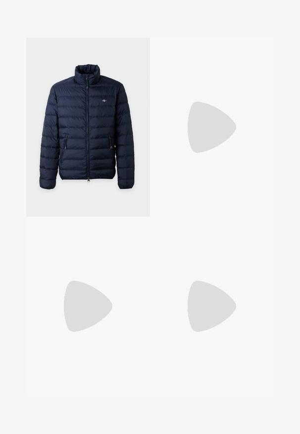 Veste matelassée bleu marine avec col montant, fermeture éclair avant, poches latérales zippées et petit logo sur la poitrine gauche.; Polo à manches longues bleu marine avec col, patte de boutonnage à deux boutons et petit logo CK rouge sur la poitrine gauche. Tissu en coton.; Jean en denim bleu clair avec une coupe droite, finition délavée, cinq poches et une fermeture à bouton. Design classique et épaisseur moyenne.; Mocassin en cuir noir flottant au-dessus d'un tapis beige avec des meubles arrondis marron en arrière-plan.
