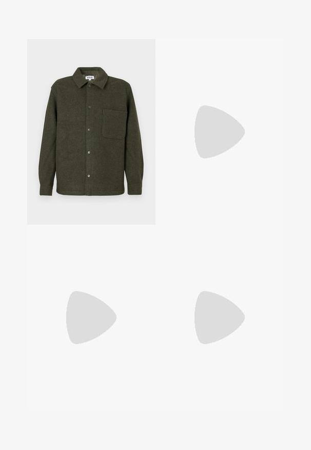 Veste chemise en laine verte avec un col, fermeture à boutons sur le devant, poche poitrine unique et manches longues. Fini lisse et texturé.; Pull beige à manches longues avec col rond, poignets et ourlet côtelés, arborant un petit emblème de tête de renard orange sur le côté gauche de la poitrine.; Pantalon en denim bleu clair avec taille haute, design à jambe droite et poches latérales accentuées. Présente des coutures visibles et une fermeture classique à boutons.; Baskets beiges en daim avec semelle en gomme, design à lacets, flottant à l'intérieur sur un sol en béton poli près d'un mur en blocs de verre.