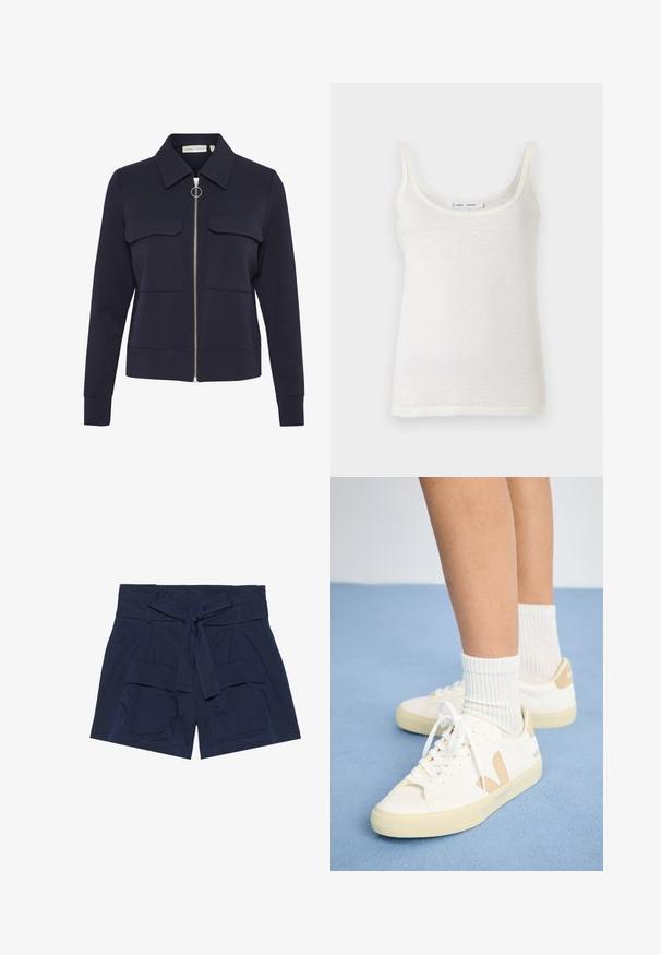 Marine blauwe ritsjack gemaakt van zachte stof met een kraag, twee voorzakken en een ronde ritstrekkertje. Gladde textuur en aansluitend design.; Witte katoenen tanktop met dunne bandjes, met een ronde hals en een licht doorschijnende textuur. De zoom is recht zonder extra accenten.; Marineblauwe shorts met een brede tailleband en een bijpassende stoffen riem, voorzien van twee grote voorzakken en zichtbare stiksels.; Witte sneakers met tan accenten, ronde neus en witte veters. Draag met geribbelde witte sokken, tegen een lichtblauwe achtergrond.