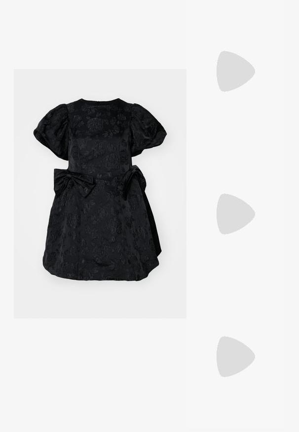 Robe noire avec des manches bouffantes, texture florale et détail en nœud à la taille. Le tissu a un léger éclat et un motif brodé.; Sandale blanche à talon à bout ouvert avec des pois noirs et des fines brides croisées sur un talon aiguille noir.; Petit sac à main noir brillant avec deux longues anses et des détails à cordon sur les côtés sur un fond clair uni.; Boucles d'oreilles créoles en argent avec trois bandes semi-circulaires superposées, dont une ornée de petits cristaux clairs sur un fond clair.