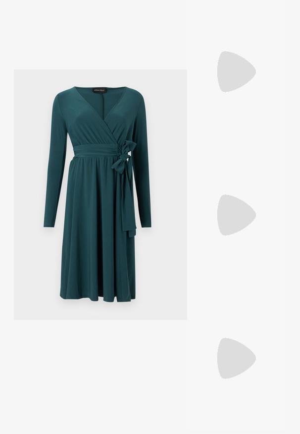 Robe portefeuille bleu sarcelle longueur genou avec manches longues, décolleté en V, taille froncée et détail nœud à nouer sur le côté.; Chaussure à talon haut en daim noir avec un bout pointu et une bride de cheville. Présente une boucle en or et un talon mince et effilé.; Sac à main en cuir vert avec poignée sur le dessus, fermoir doré et bandoulière amovible sur un fond uni clair.; Boucles d'oreilles en métal doré avec une forme lisse et arrondie et une finition polie. Design simple sans embellissements supplémentaires.