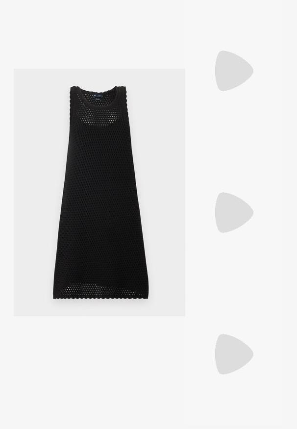 Robe noire sans manches en maille avec un col rond et un motif ajouré, longueur genou avec bords festonnés.; Jambes portant des leggings côtelés foncés associés à des ballerines noires avec de petits détails en nœud sur fond blanc.; Sac à main en cuir noir de forme triangulaire, avec une grande poignée découpée et des coutures détaillées le long des bords. Texture lisse.; Boucles d'oreilles argentées en forme d'étoile, avec une surface lisse et brillante. Chaque boucle d'oreille possède cinq pointes et des détails subtils de texture de surface.