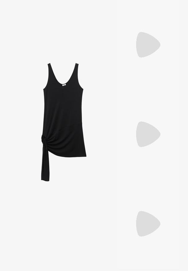 Débardeur noir sans manches avec encolure dégagée et détail nœud en tissu en bas à gauche.; Jambes portant des leggings côtelés foncés associés à des ballerines noires avec de petits détails en nœud sur fond blanc.; Petit sac à main noir brillant avec deux longues anses et des détails à cordon sur les côtés sur un fond clair uni.; Boucles d’oreilles créoles en métal argenté avec une surface lisse légèrement incurvée et des fermoirs à clapet sur un fond blanc uni.