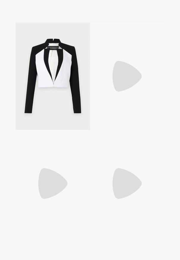 Blazer court avec des panneaux noirs et blancs, manches longues et fermeture éclair à l'avant. Présente un col cranté et une texture de tissu lisse.; Robe sans manches longueur genou avec sur-couche asymétrique noire sur le haut et jupe blanche, encolure ronde et fermeture éclair au dos.; Bottine en cuir noir avec bout pointu et petit talon, présentée devant un mur en blocs de verre et un sol poli.; Sac à main en cuir noir et blanc avec poignée supérieure, bandoulière réglable et logo métallique stylisé sur le rabat avant.