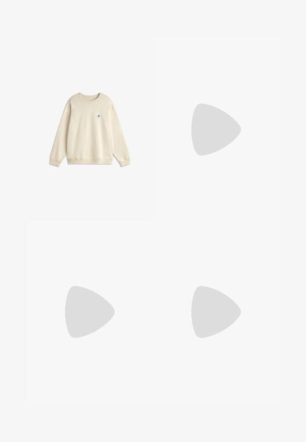 Sweat-shirt beige à manches longues et col rond avec poignets et ourlet côtelés, présentant un petit logo circulaire bleu sur la poitrine gauche.; Chemise blanche à manches longues, en coton. Présente un col classique, des boutons sur le devant et une texture lisse sans motifs visibles.; Short gris clair avec des rayures verticales blanches et beiges, taille élastique et coupe aux genoux.; Mocassin en cuir noir avec pompons flottant au-dessus d'un tapis beige avec un canapé beige en arrière-plan.