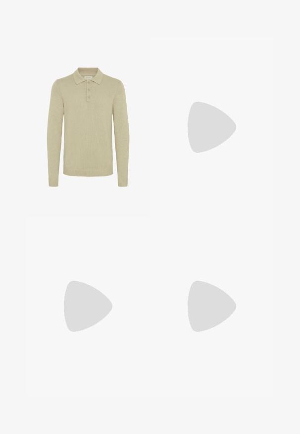 Pull en polo beige à manches longues en tissu tricoté côtelé, avec une patte de boutonnage à trois boutons et des poignets et un ourlet côtelés. Design de col classique.; Chemise blanche à manches longues avec poche avant, col boutonné et étiquette de marque visible à l'intérieur du col.; Jean en denim bleu foncé avec une coupe droite, design à cinq poches, bouton en métal et fermeture éclair, et motifs de décoloration légère.; Un seul mocassin en cuir brun foncé flottant au-dessus d’un tapis texturé beige, avec un canapé beige flou en arrière-plan.
