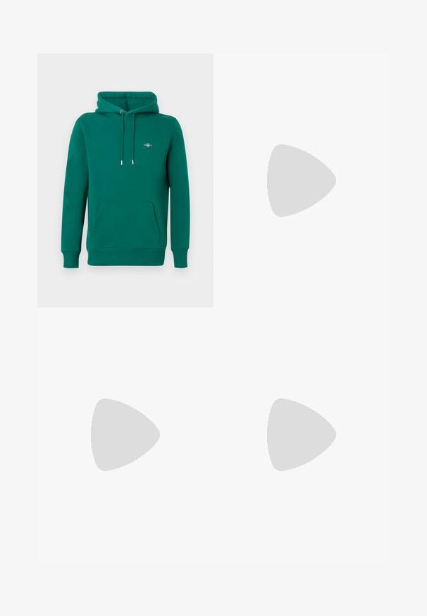 Sweat à capuche vert avec poche avant, capuche à cordon, poignets côtelés et logo brodé sur la poitrine. Fabriqué en matériau doux et confortable.; Polo blanc à manches courtes avec col, patte de boutonnage à trois boutons et petit logo gris Calvin Klein sur la poitrine gauche.; Jean droit en denim bleu clair avec taille haute, cinq poches, fermeture à boutons et léger délavage sur les cuisses et les genoux.; Mocassin beige en daim à enfiler avec coutures visibles et semelle claire, positionné au-dessus d'un tapis crème, avec un meuble translucide orange en arrière-plan.