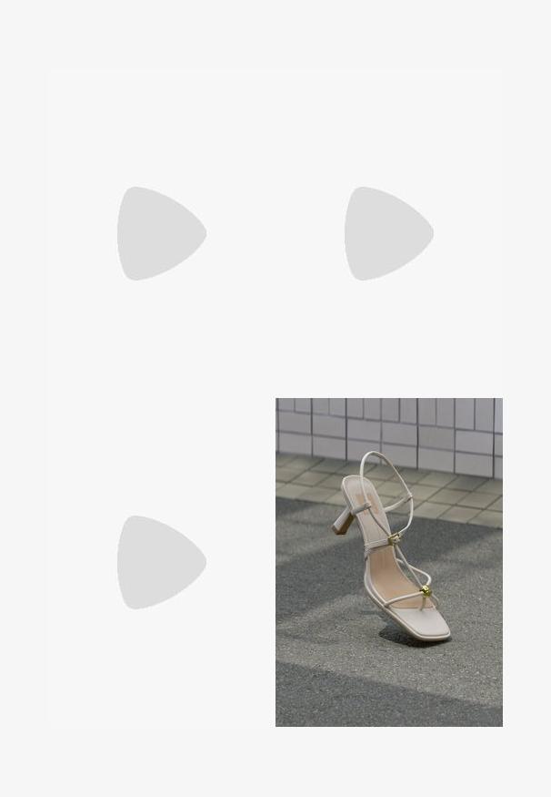 Grønne buksedragt med tynde stropper, indsnøring i taljen og brede bukseben. Lavet af et letvægtsmateriale med en glat tekstur.; Beige sandal med hæl og stropper, guldspænde og dekorativ guldkugle, på brostensbelagt underlag nær flisebelagt væg.; Cremefarvet blødt læder håndtaske med indsamlet design, sølvramme-lukkemekanisme, kort hank og aftagelig kæderem.; Sølv clip-on øreringe med spiralmønster, der har en glat metallisk tekstur og runde former. Ingen synlige udsmykninger eller mønstre.