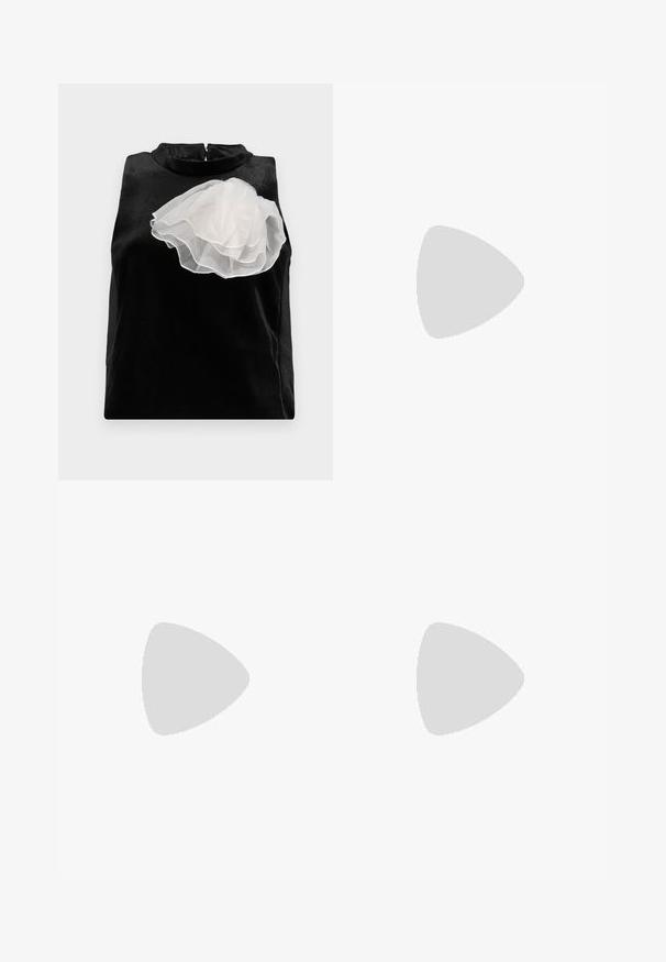 Sort ærmeløs top lavet af glat stof med en stor hvid tuleblomstaccent på venstre side og en høj halsudskæring med lynlås.; Sort nederdel lavet af glat stof, med et oversized draperet design på den ene side, der danner en høj-lav kant.; Sort læder højhælet sko med spids tå og metal-sølv hætte. Har en glat finish og en slank hæl på 10 cm.; Sort clutchtaske med frynser, sølvlukning og kæderem mod en ensartet lys baggrund.