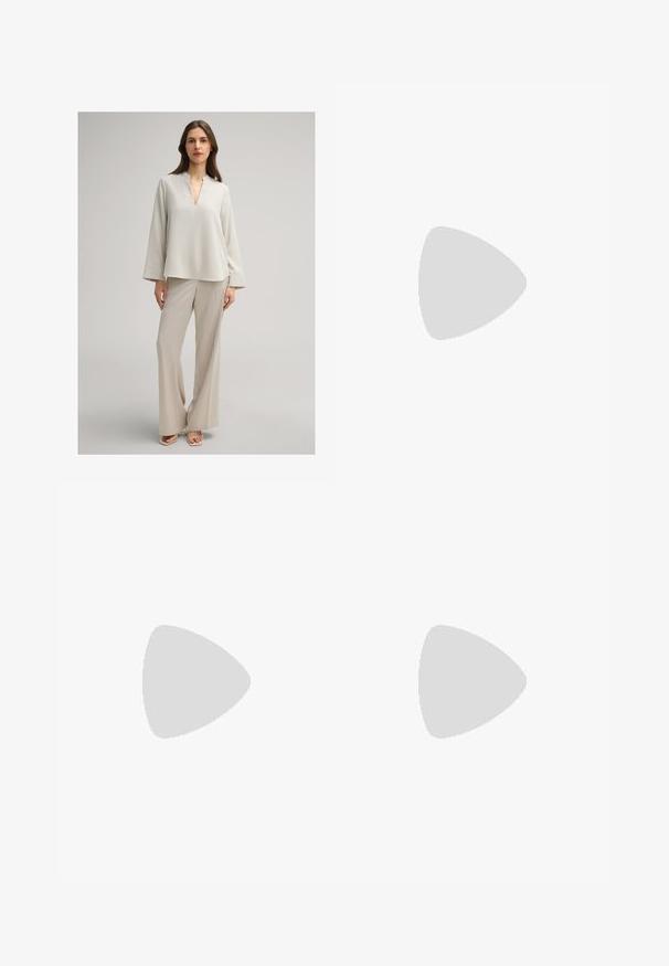 Femme debout portant un chemisier ample beige clair à manches larges et un pantalon large assorti sur fond uni.; Jupe crayon beige à mi-longueur, en tissu côtelé, dotée d'un design drapé à l'avant et d'une fermeture éclair sur le côté en argent. Texture lisse.; Chaussure à talon haut beige à bout pointu avec un talon aiguille mince sur un fond blanc uni.; Pochette en cuir beige avec rabat avant et fermeture par sangle verticale, sur un fond clair uni.