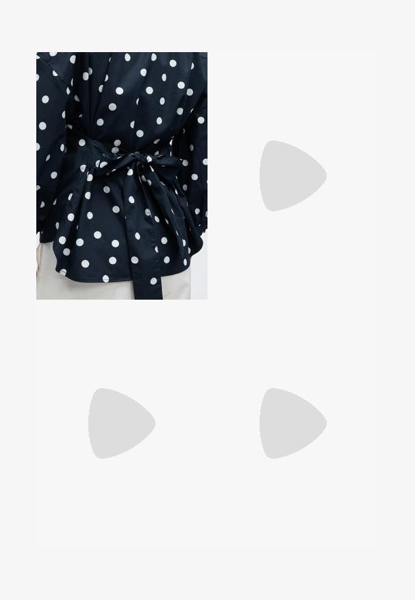 Gros plan d'un vêtement noir à pois blancs noué à la taille avec un nœud, montrant une partie des manches et de l'ourlet inférieur.; Pantalon noir taille haute à jambes larges avec plis et une fine ceinture tressée marron, présenté sur un fond blanc.; Ballerines en cuir verni noir avec un bout pointu, un petit nœud à l'avant et un petit talon carré. Texture lisse et brillante.; Sac hobo en cuir couleur crème avec une seule bandoulière, texture lisse et un détail de fermoir doré à l'avant.
