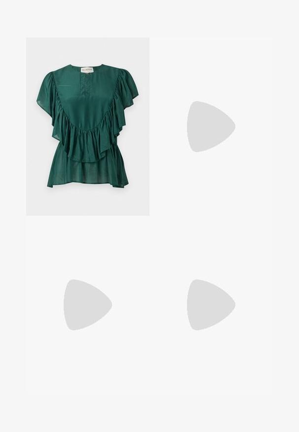 Blouse vert foncé à manches courtes avec des détails volantés le long de la poitrine et des manches, et une petite fermeture éclair à l'avant sous l'encolure.; Pantalon large à taille élastique ; jambe gauche bleue avec un imprimé cachemire doré, jambe droite rose avec un motif losange géométrique rouge.; Sandale en cuir noir avec talon bas flottant au-dessus d'un tapis beige près d'une table ronde marron dans un cadre intérieur minimaliste.; Petite pochette tissée marron avec cadre métallique argenté, deux fermoirs ronds en bois, et une courte chaîne argentée sur fond blanc.