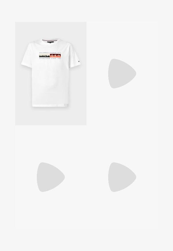 Hvid kortærmet bomulds T-shirt med "Hilfiger" tekst i blokfarver, "Columbus Avenue NYC" ovenover, og "Etableret siden 1985" nedenfor.; Lysblå denimjeans med lige ben, femlommesdesign og let slid. Inkluderer metalknap og lynlås lukning.; Sort lædersko i loafer-stil svæver over et beige tæppe med et blankt brunt rundt bord i baggrunden.; Sølv kædedyse med et lion-hoved vedhæng, som har udsøgt detaljering, glitrende accenter og et klassisk kæde-design.