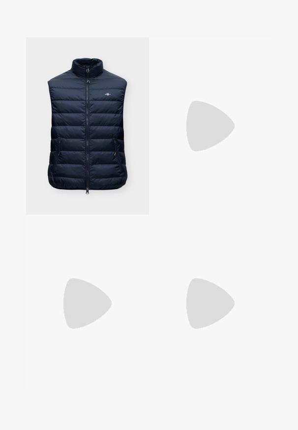 Veste sans manches matelassée bleu marine avec col montant, fermeture éclair à l'avant, deux poches latérales zippées et petit logo sur la poitrine.; Pull col rond bleu marine foncé à manches longues avec petit logo Tommy Hilfiger rouge, blanc et bleu sur la poitrine et à l’intérieur du col.; Jean denim bleu foncé à jambes droites, cinq poches et fermeture à bouton à la taille, présenté à plat sur fond blanc.; Baskets en cuir blanc avec doublure intérieure noire, fermeture à lacets plats et détail logo visible. Semelle en caoutchouc texturée pour une meilleure adhérence.
