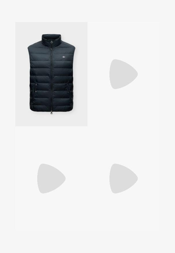 Veste sans manches matelassée noire avec col montant, fermeture éclair frontale, deux poches zippées et petit logo sur la poitrine.; Polo à manches courtes de couleur vert foncé, en tissu tricoté texturé, avec un col classique et une encolure en V. Silhouette simple et élégante.; Jean en denim bleu clair à coupe droite, fermeture avant par bouton et zip, passants de ceinture et cinq poches, dont un petit logo sur la poche droite.; Baskets décontractées beige avec des détails en mesh et en suède, semelle blanche, flottant au-dessus d'un tapis beige texturé dans un salon moderne.