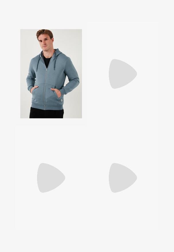 Lichtblauwe ritssluiting hoodie van zacht materiaal. Beschikt over een trekkoordcapuchon, voorzakken en geribbelde manchetten met een logo-label aan de onderkant.; Witte korte mouwen T-shirt met ribbelstructuur. Ronde hals, ontspannen pasvorm, geen zichtbare patronen of accenten. Eenvoudig en veelzijdig ontwerp.; Beige loungebroeken met een elastische tailleband en trekkoord, met een recht model en een zachte, gladde textuur.; Witte leren sneaker met een glad oppervlak, ronde neus en platte witte veters. Voorzien van een gestructureerde rubberen zool en minimale ontwerpelementen.